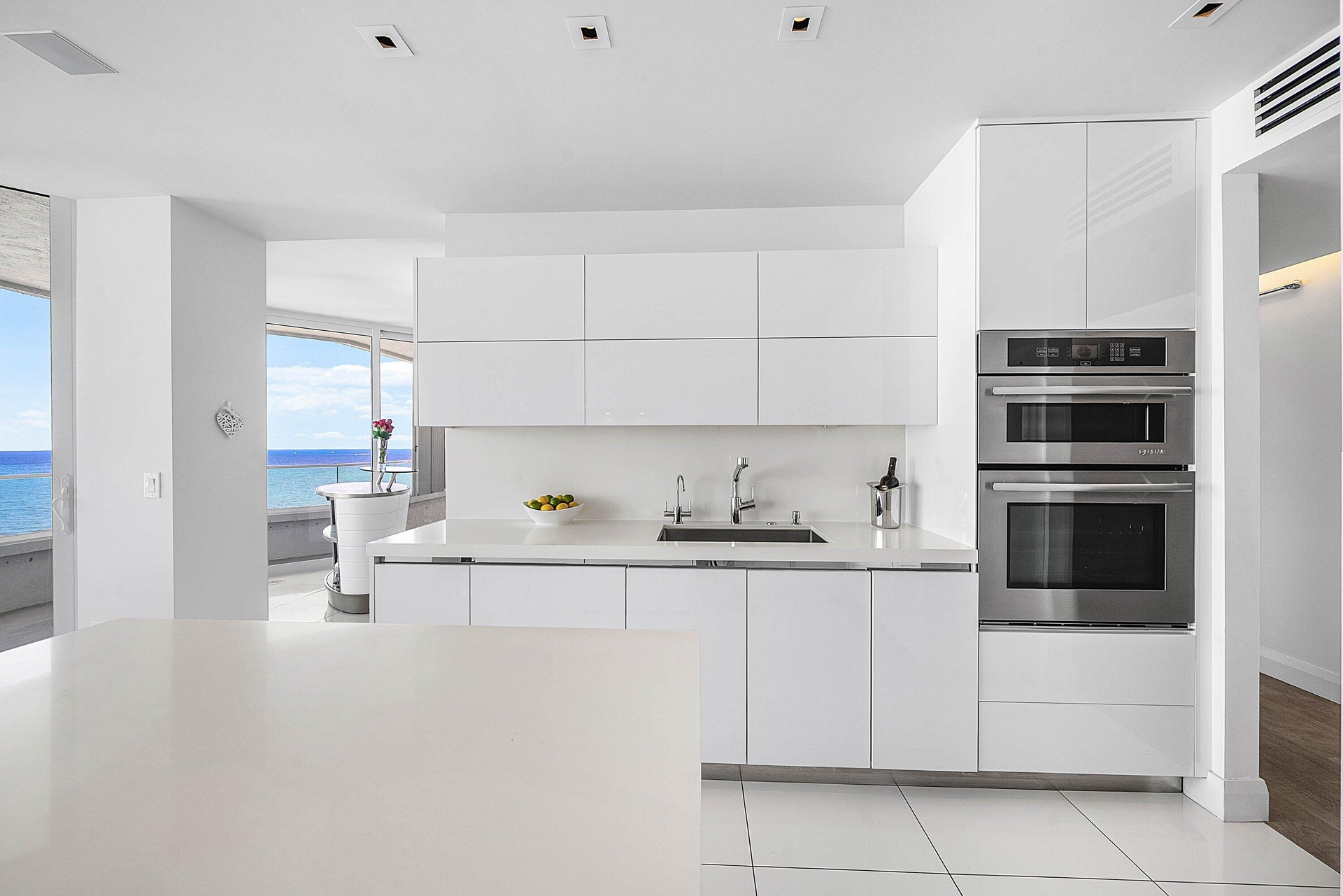 Contemporary kitchen featuring high-gloss white cabinetry, integrated stainless steel double wall ovens, solid-surface countertops, recessed ceiling l