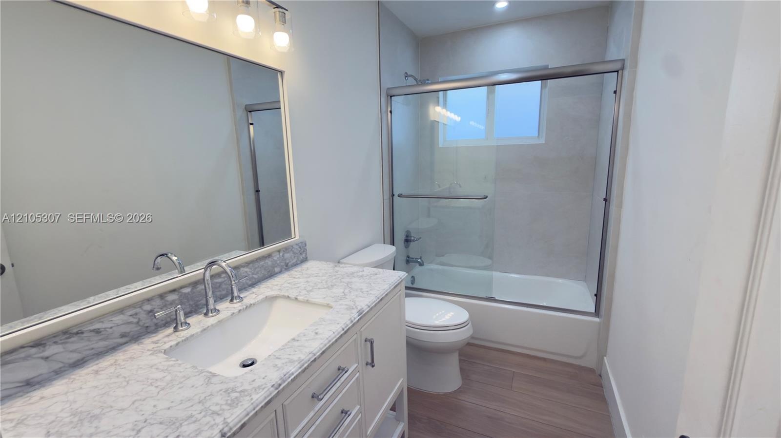 Bathroom with tub, eaturing a vanity with a stone-finish countertop, undermount sink, chrome faucet, large wall-mounted mirror with integrated lightin