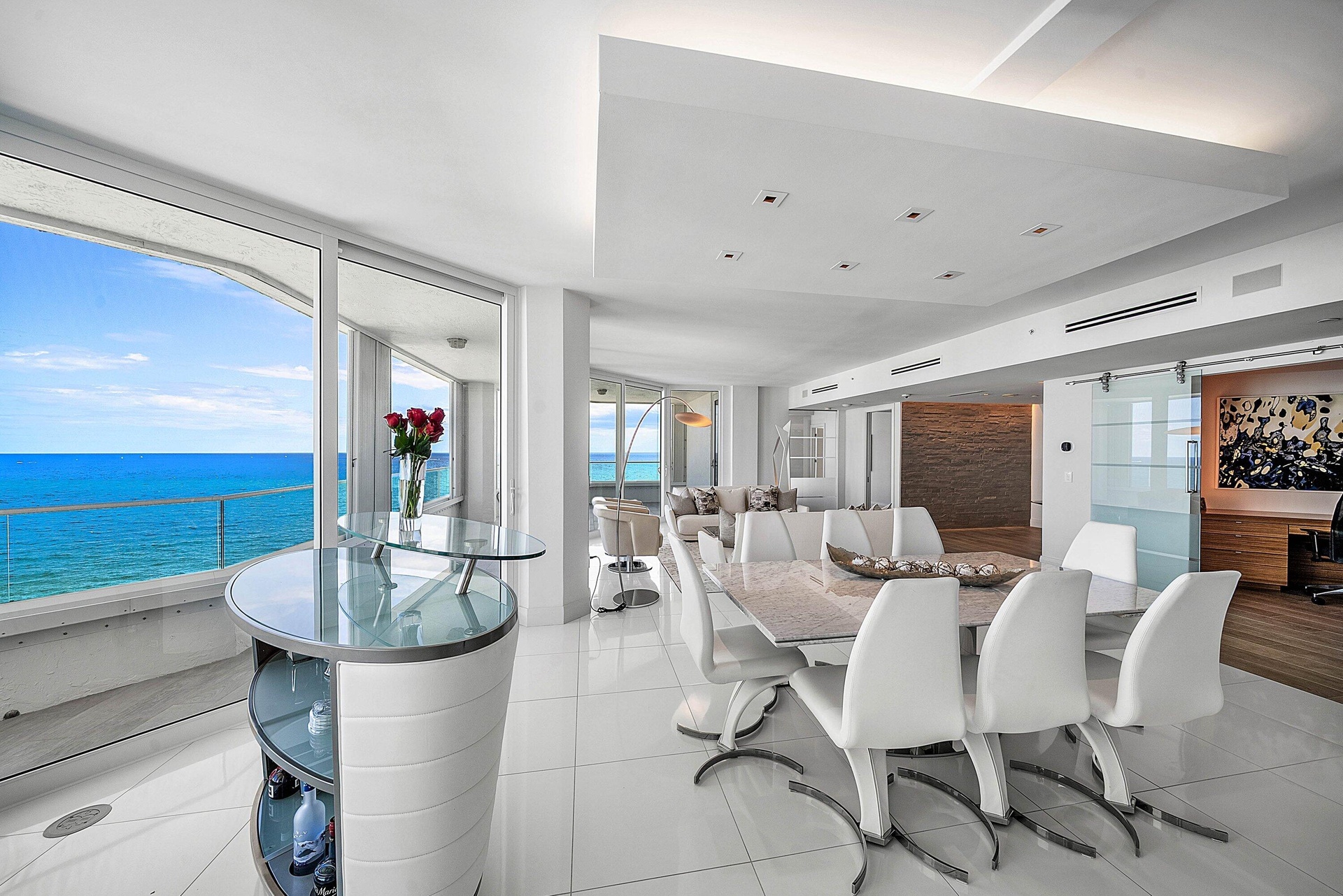 Expansive floor-to-ceiling windows, polished tile flooring, tiered tray ceiling with recessed lighting, integrated glass and stone-finish bar, and sli