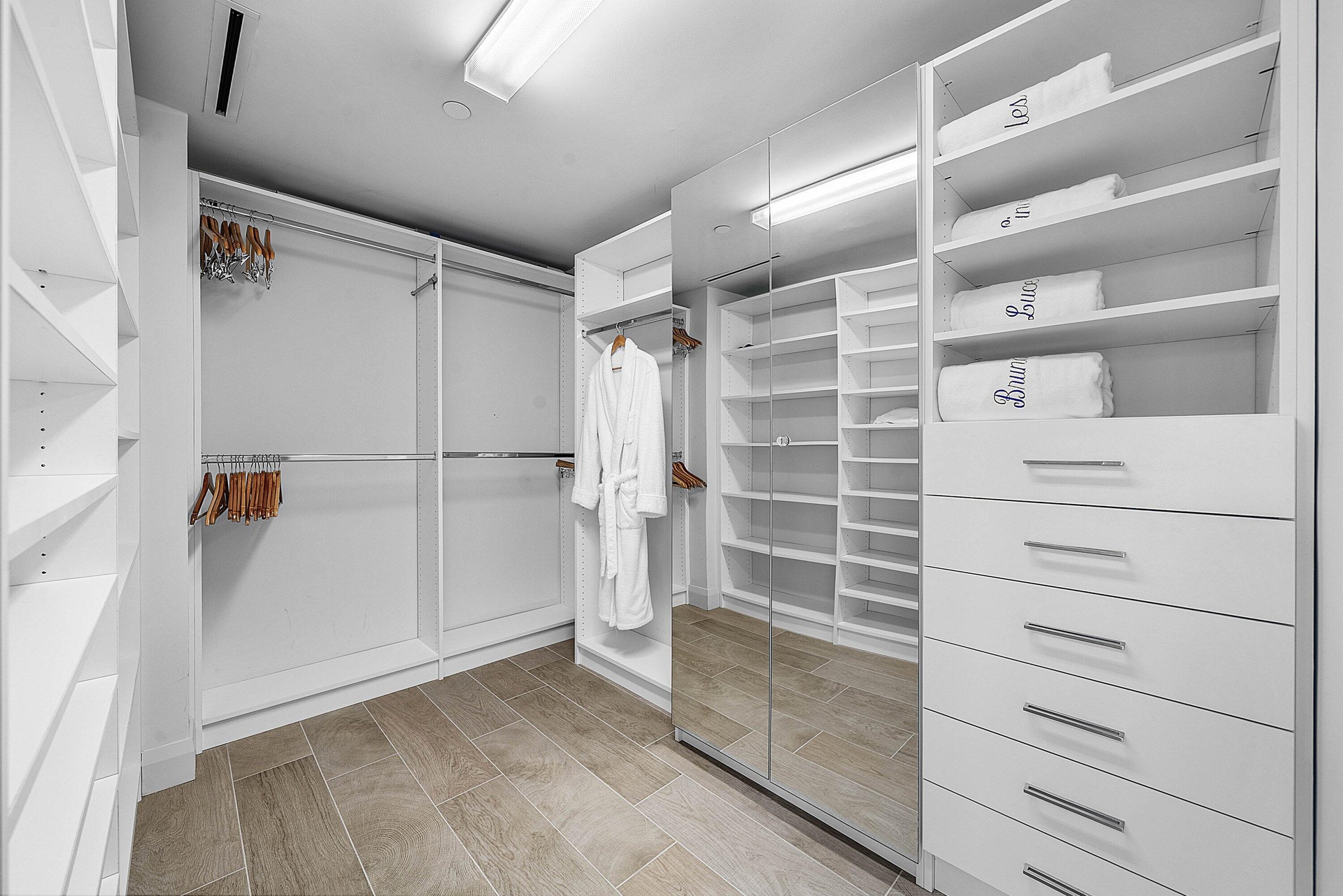 Custom storage system featuring floor-to-ceiling white cabinetry, multi-level hanging rods, built-in shelving, integrated mirror panels, and wood-fini