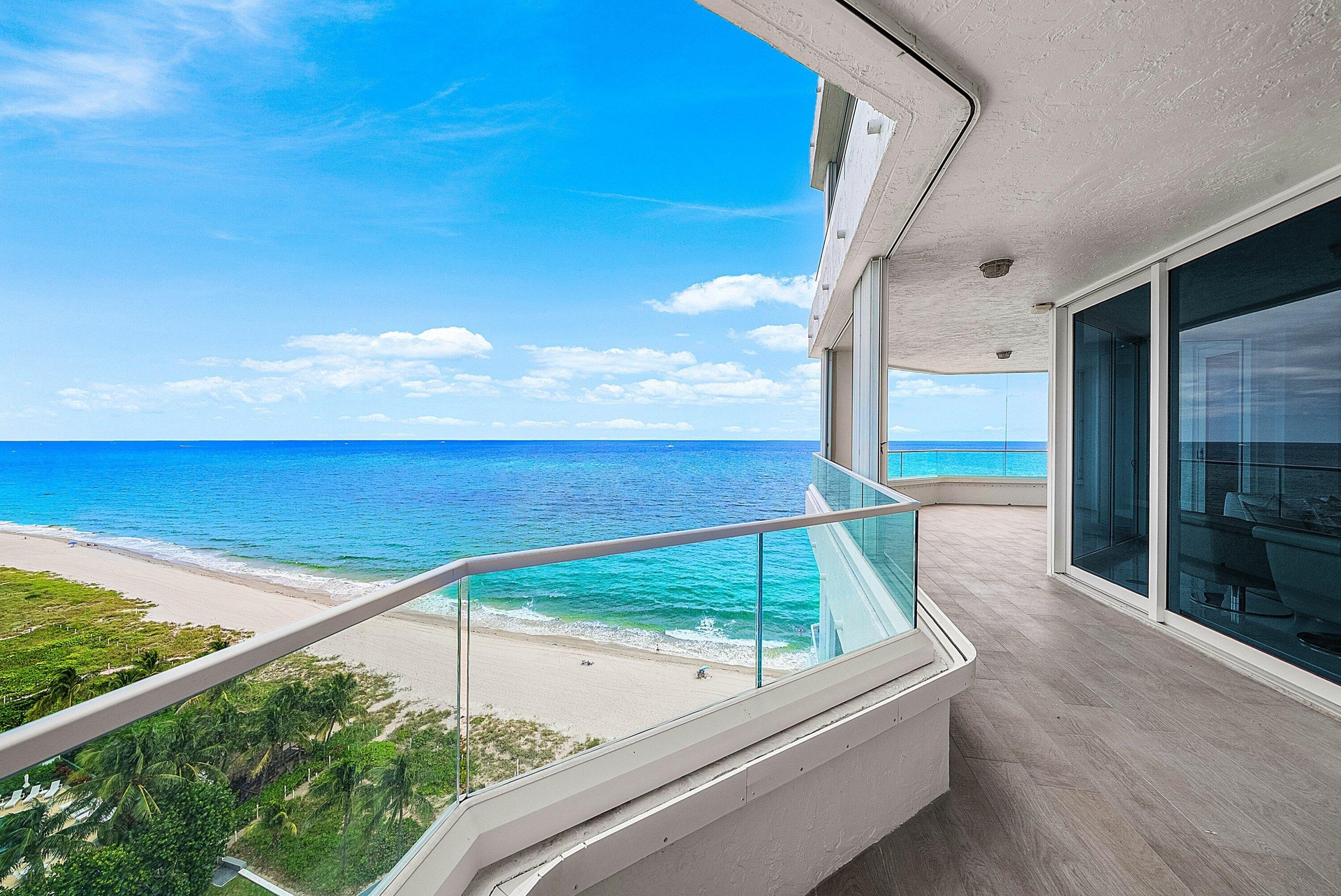 Wrap-around balcony featuring glass panel railings, wood-finish flooring, and floor-to-ceiling sliding glass doors