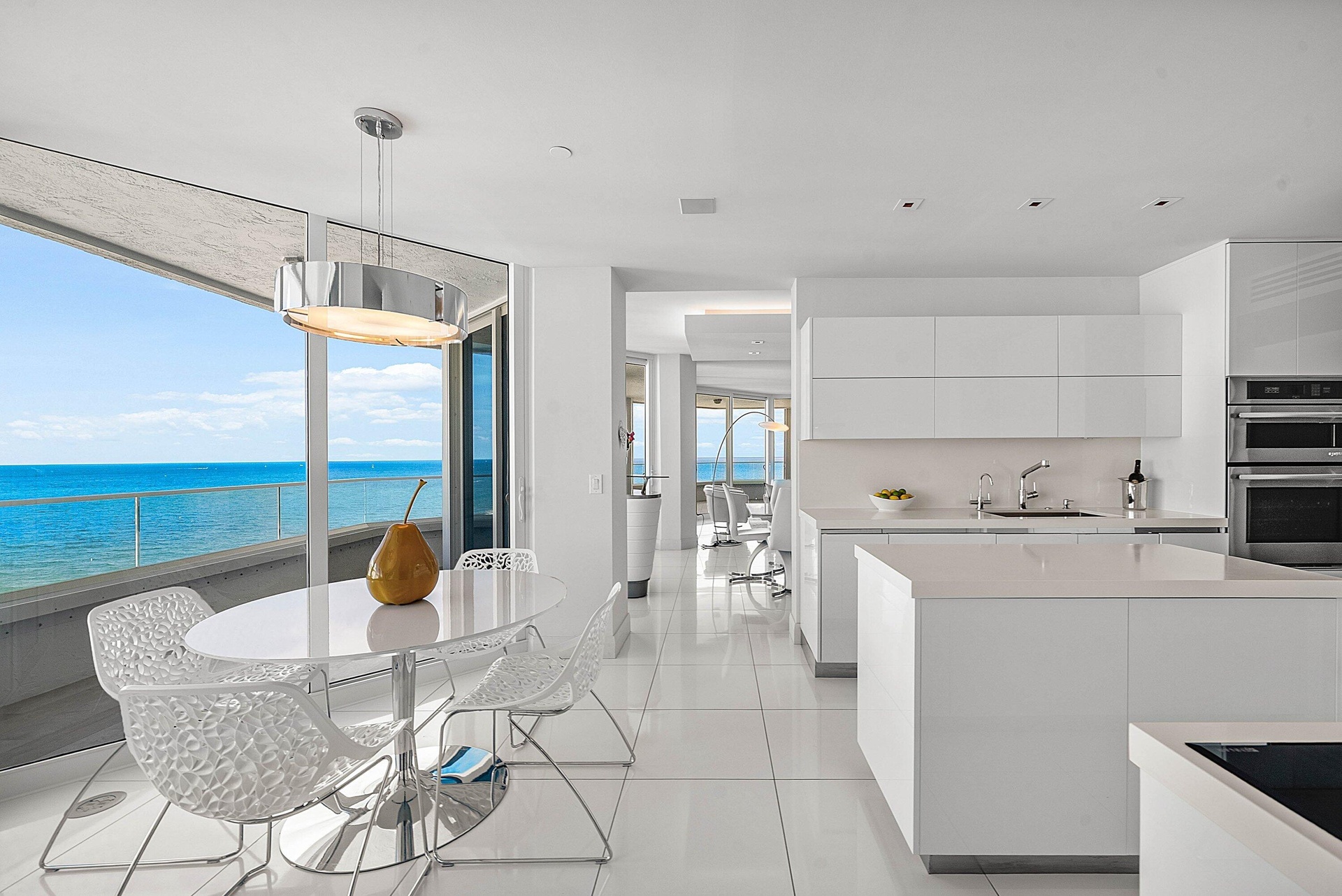 Floor-to-ceiling glass paneling, high-gloss white cabinetry, center island with stone countertop, large-format tile flooring, and integrated stainless