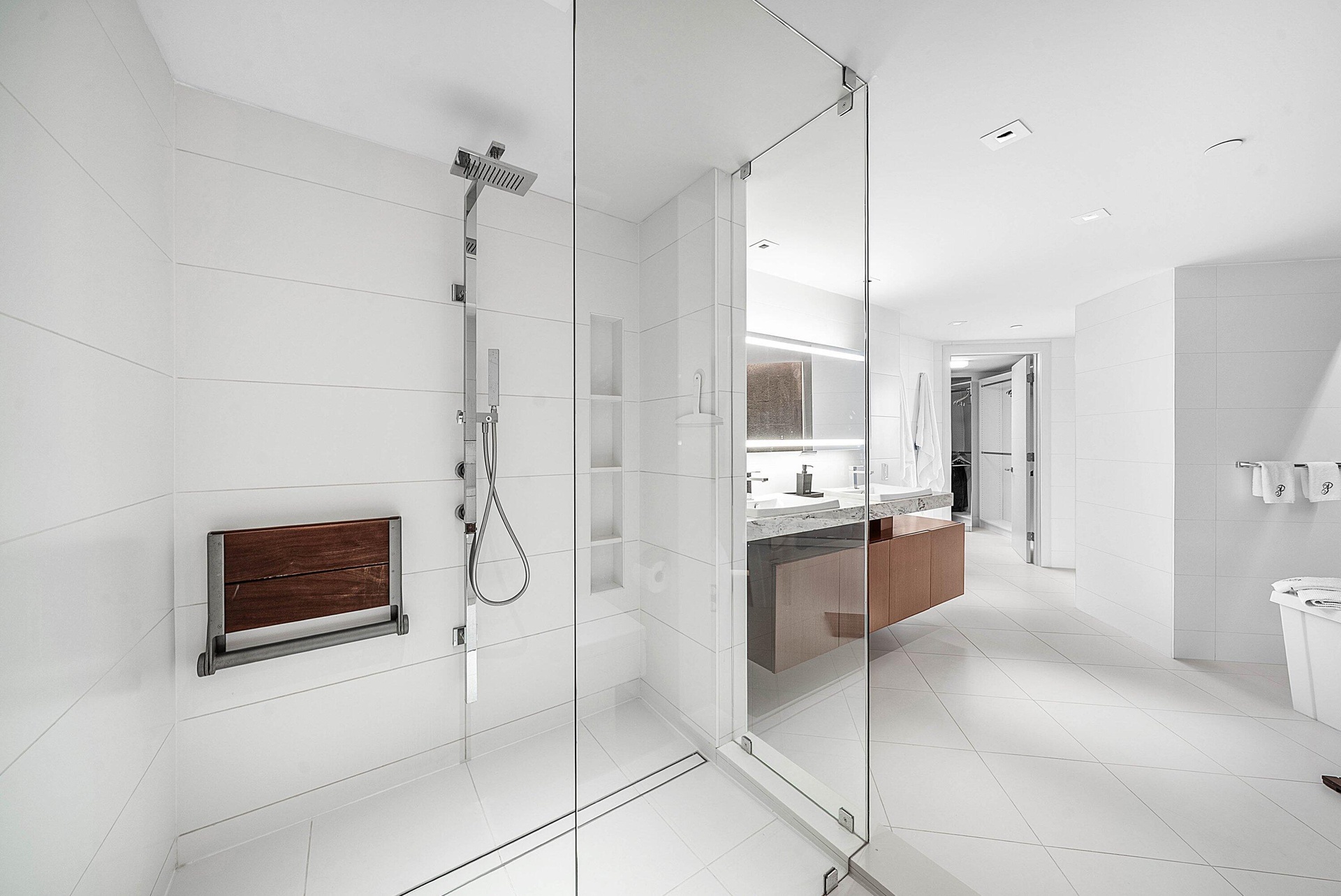Walk-in shower with floor-to-ceiling tile, frameless glass enclosure, wall-mounted shower panel with handheld sprayer, built-in shelving, and integrat