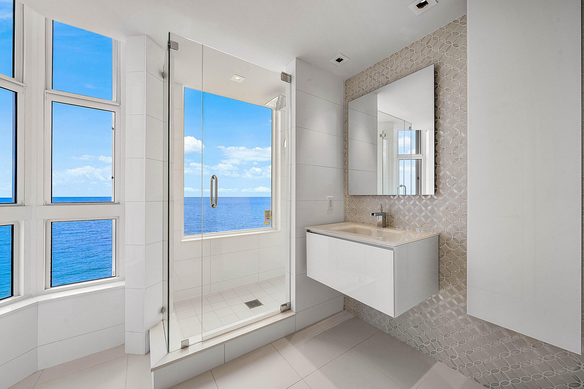 Glass-enclosed shower with integrated window, floating vanity, wall-mounted mirror, mosaic tile accent wall, and floor-to-ceiling windows with water b