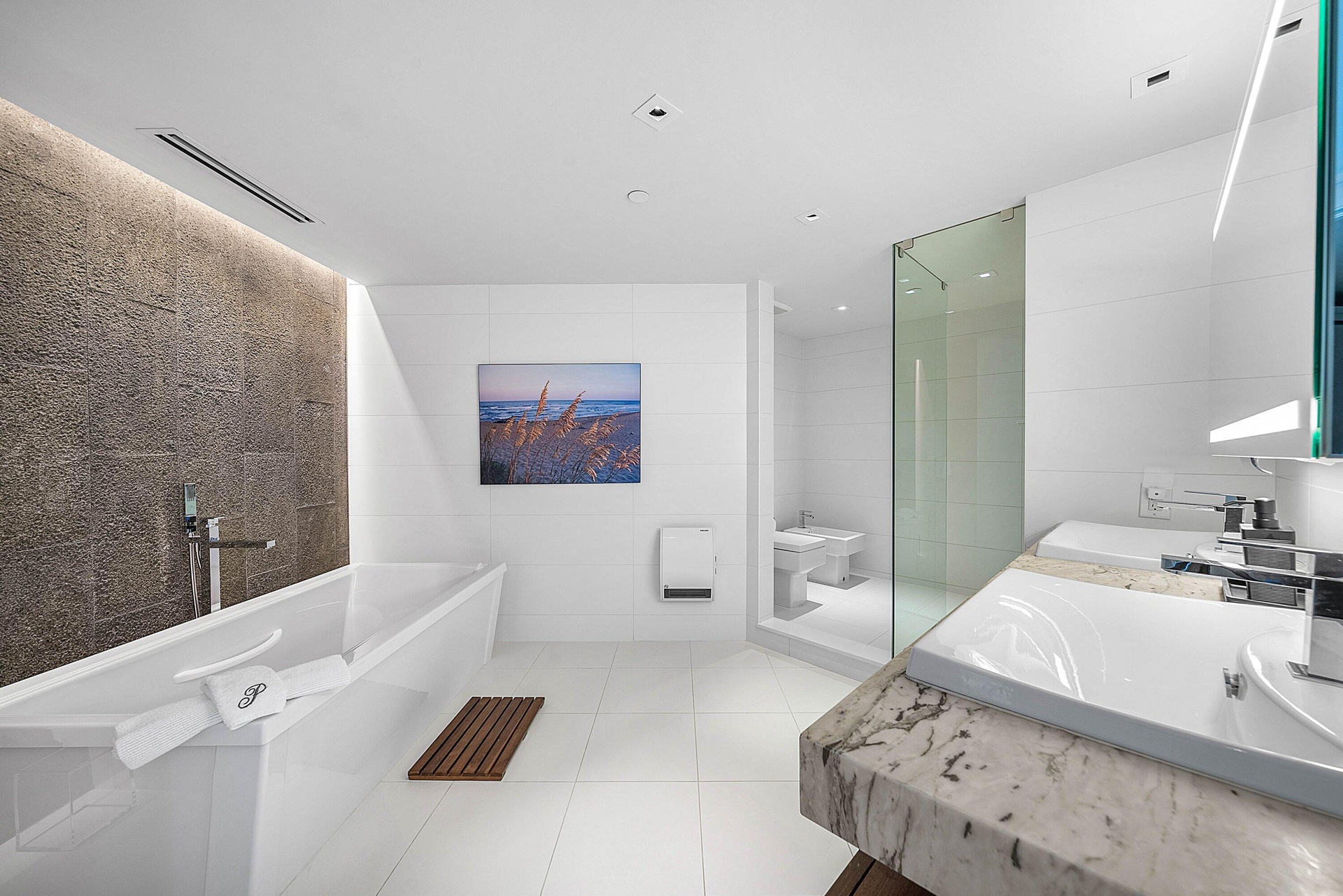 Bathroom featuring a freestanding white soaking tub, textured stone accent wall, dual-sink vanity with stone countertop, frameless glass-enclosed show