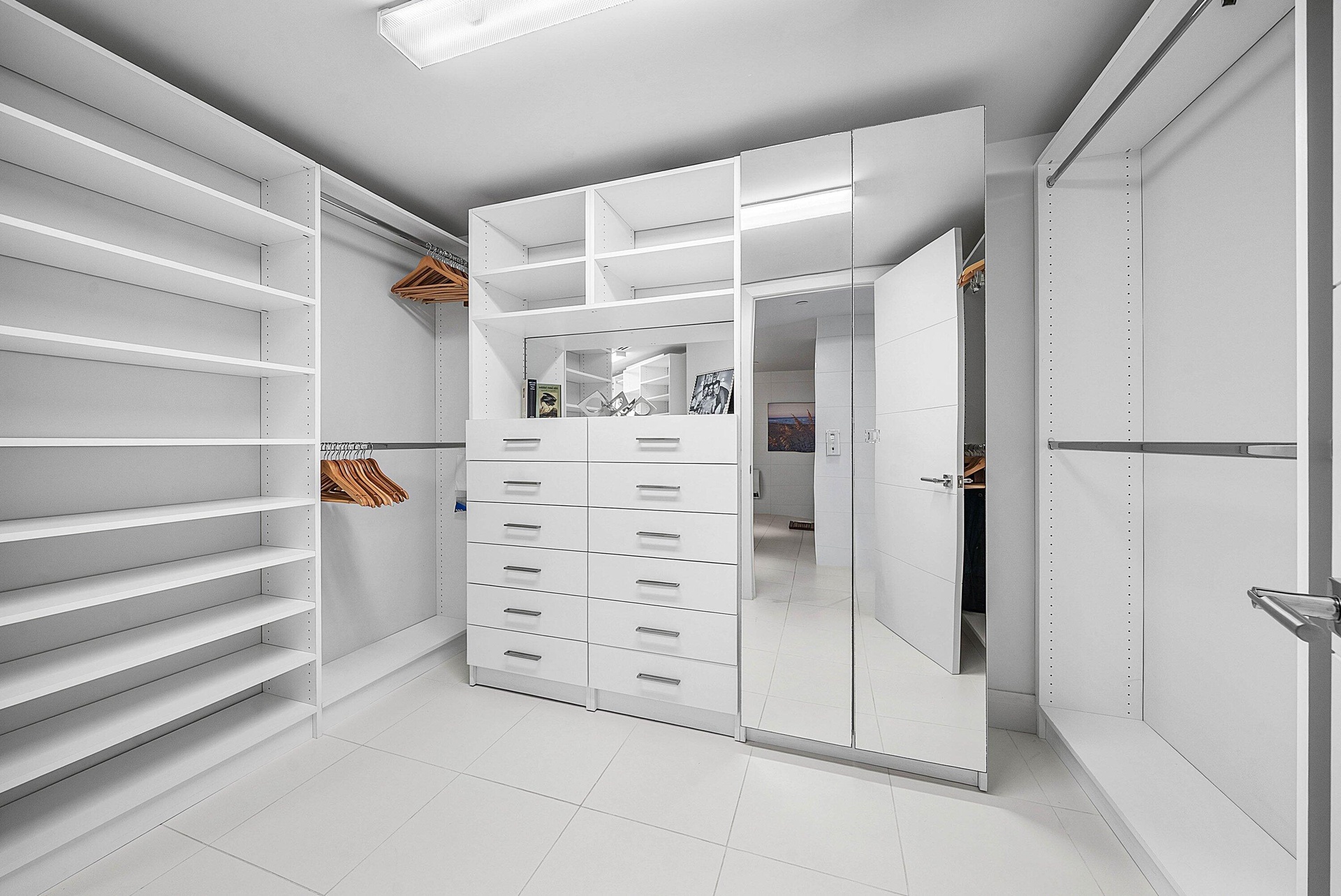 Custom storage closet featuring floor-to-ceiling white shelving, integrated multi-drawer cabinetry, full-length mirror panels, and metallic hardware