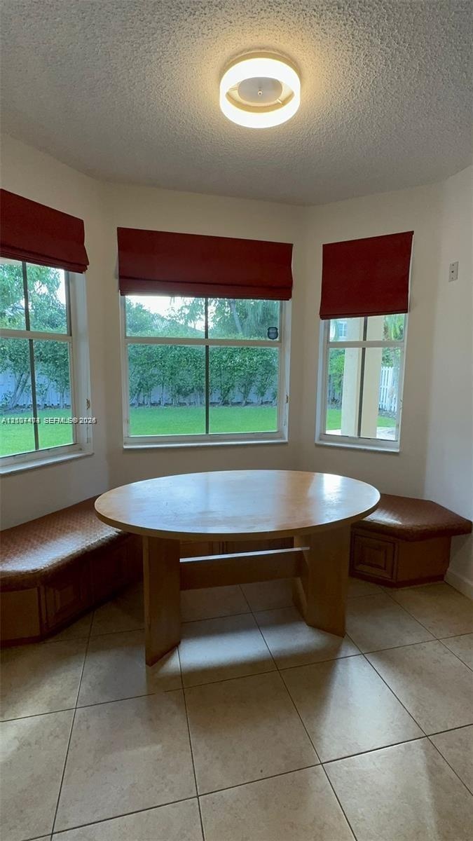 Bay window featuring built-in wooden bench seating, neutral floor tile, and a flush-mount overhead light fixture