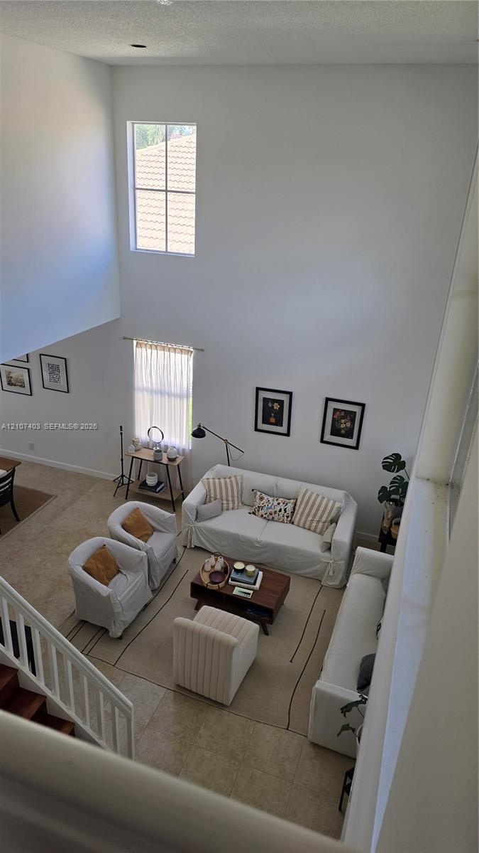 High-ceiling interior featuring multi-level windows, neutral tile flooring, and white spindle staircase railing