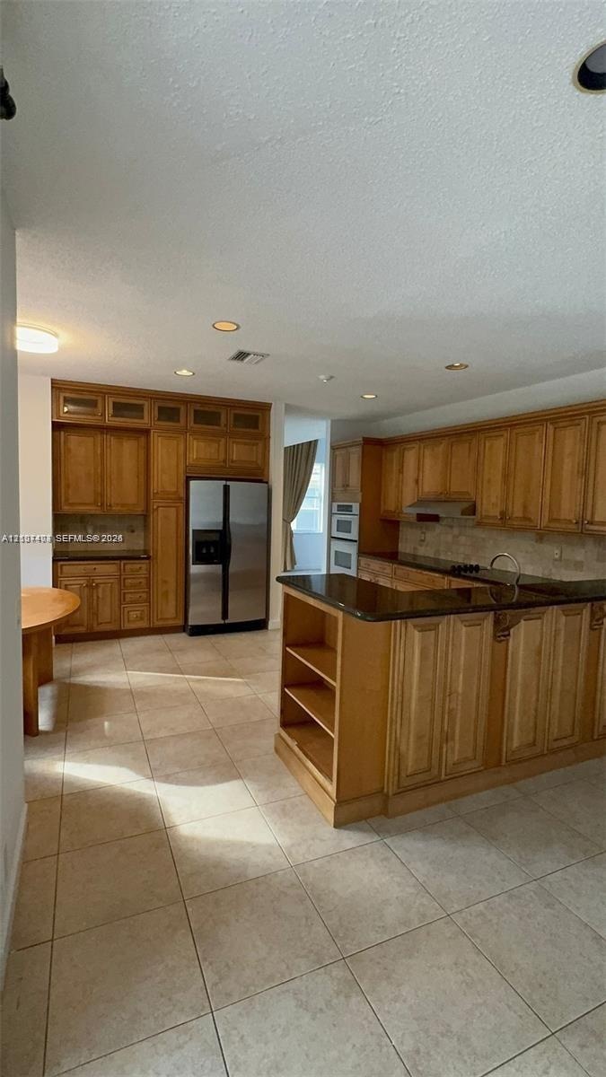 Kitchen featuring extensive wood cabinetry, dark stone countertops, tile flooring, recessed lighting, and built-in appliances