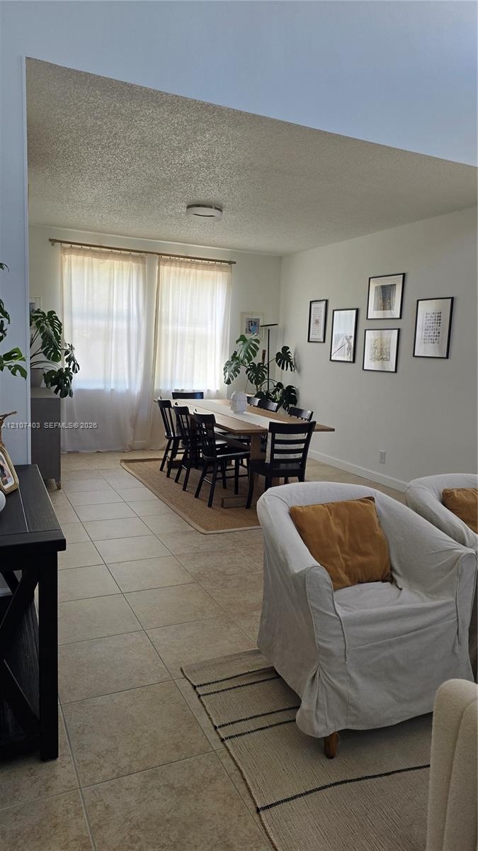 Open-concept living space featuring high vaulted ceilings, large windows with natural light, and neutral tile flooring throughout
