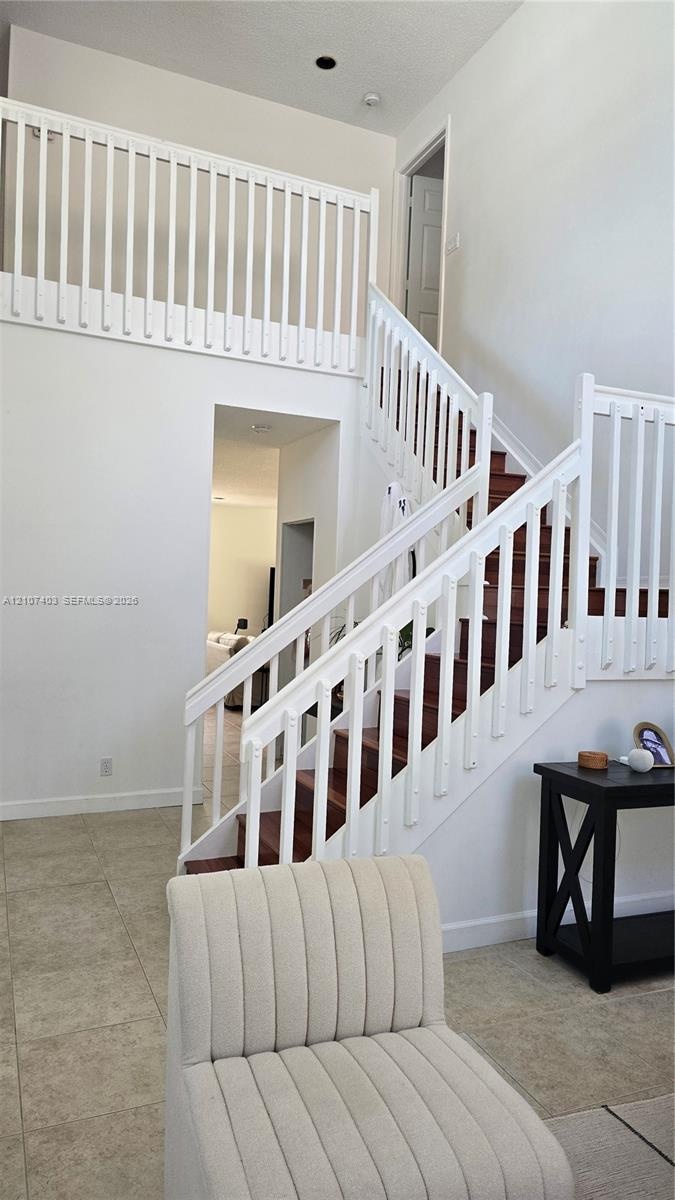 High-ceiling foyer featuring a staircase with wood-finish treads, white railings, and tile flooring