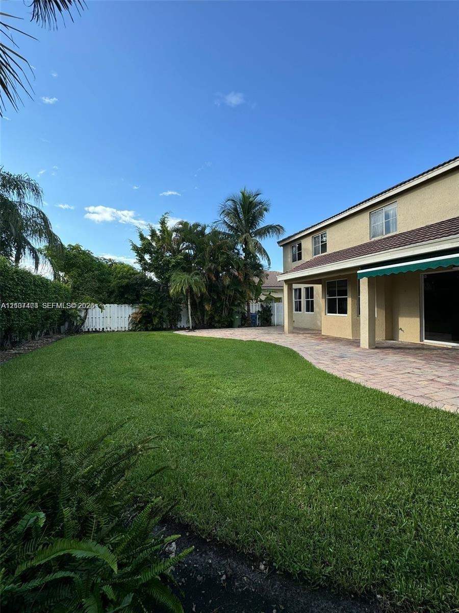 Expansive backyard featuring a manicured lawn, paver patio, attached retractable awning, and perimeter privacy fencing
