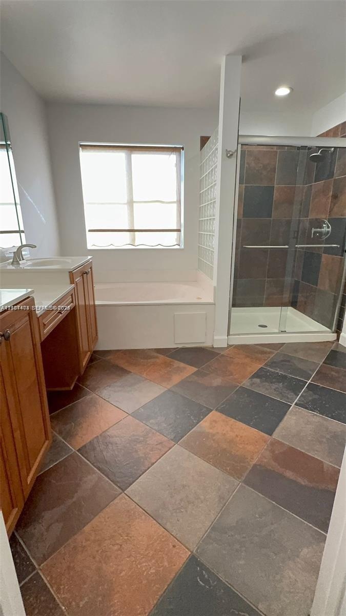 Bathroom featuring wood-finish cabinetry, a white countertop with an integrated sink, a deep soaking tub, a multi-tone tile floor, and a walk-in showe