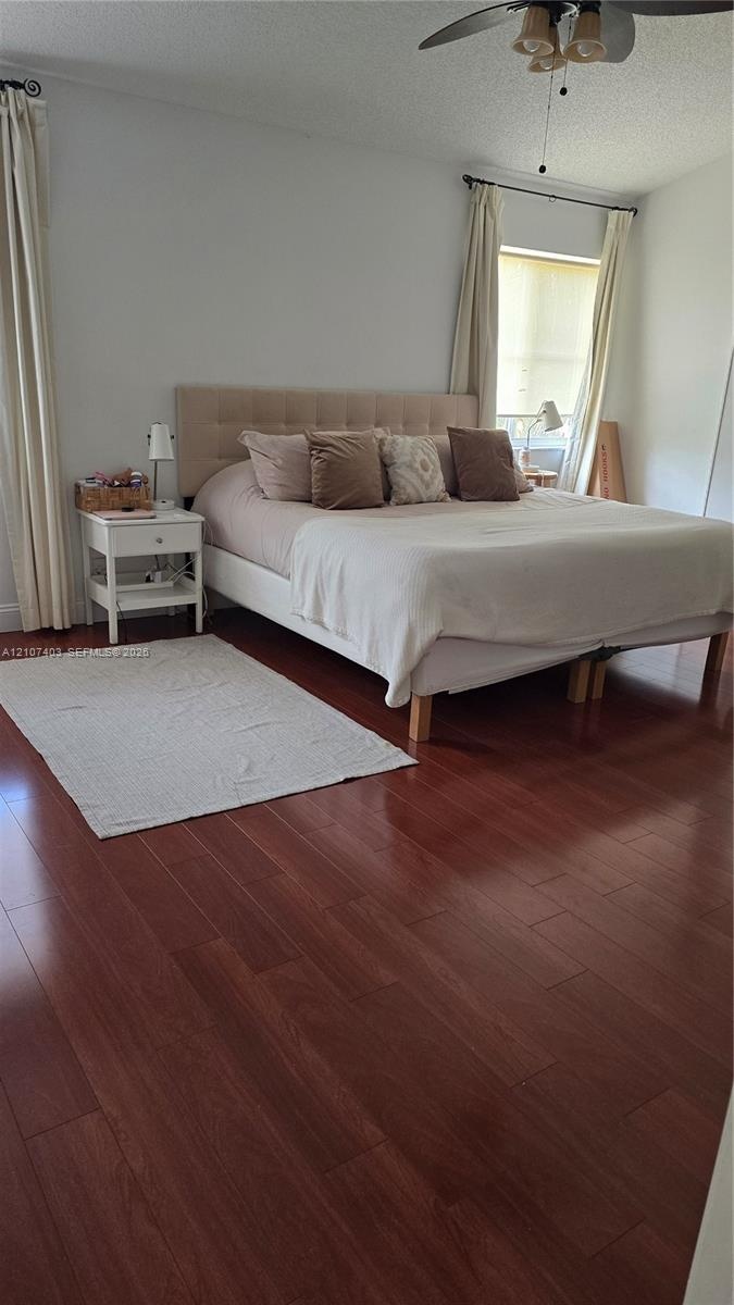 Bedroom featuring wood-finish flooring, a ceiling fan with integrated lighting, and window treatments