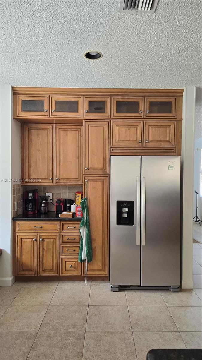 Custom built-in cabinetry featuring glass-panel upper doors, integrated stainless steel side-by-side refrigerator, stone-surfaced countertop, and tile