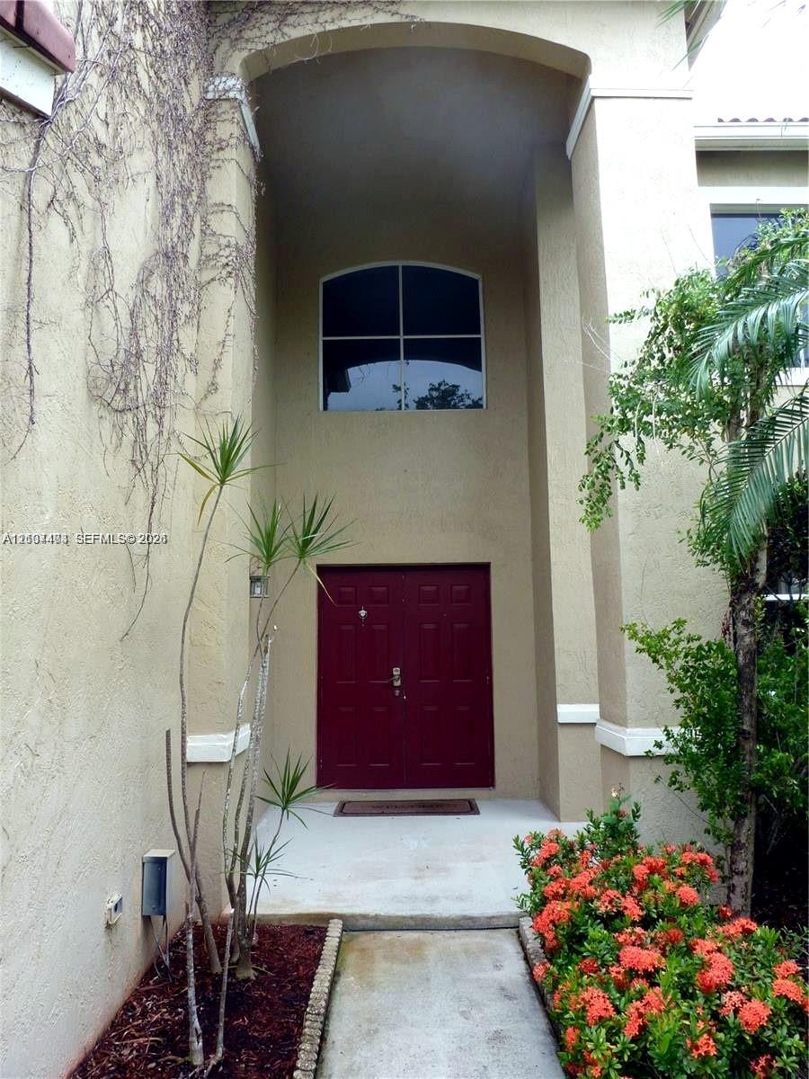 Stucco exterior entrance featuring a double door entry, covered recessed portico, arched transom window, and concrete walkway