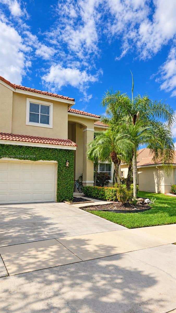 Stucco exterior with a tiled roof, integrated garage, concrete driveway, and manicured landscaping featuring mature palm trees