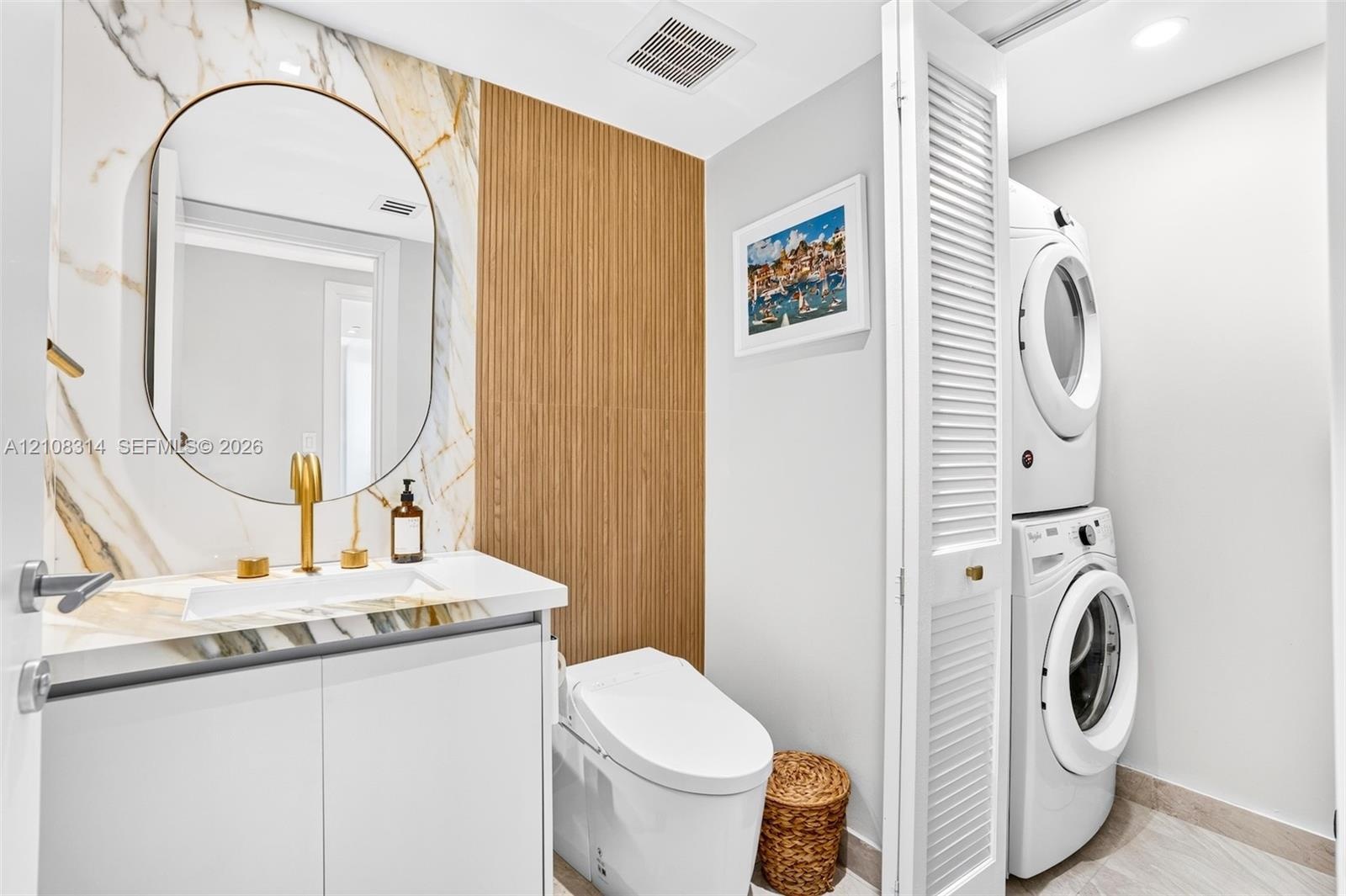 Stone-surround vanity with a circular mirror and gold-tone faucet, complemented by vertical slat wood-finish wall paneling, a low-profile toilet, and 
