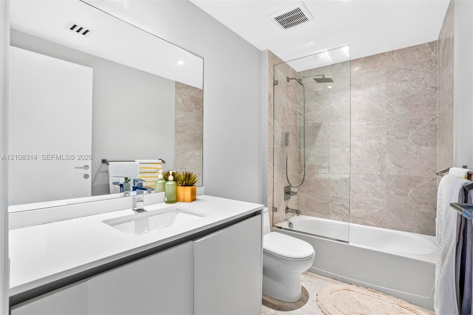 Bathroom featuring a floating vanity with a stone countertop, an integrated rectangular sink, a frameless glass shower panel, and stone-tile tub surro