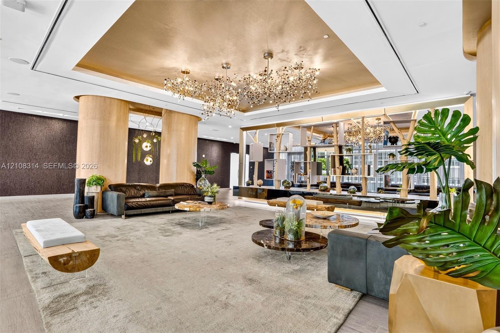 Metallic tray ceiling, large-scale multi-bulb crystal chandeliers, curved light-wood structural columns, integrated architectural shelving, and recess