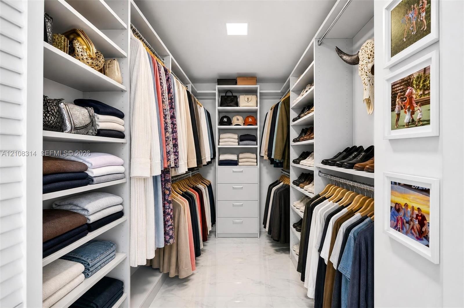 Custom walk-in closet featuring extensive built-in white shelving, integrated clothing rods, a central storage tower with four pull-out drawers, and p
