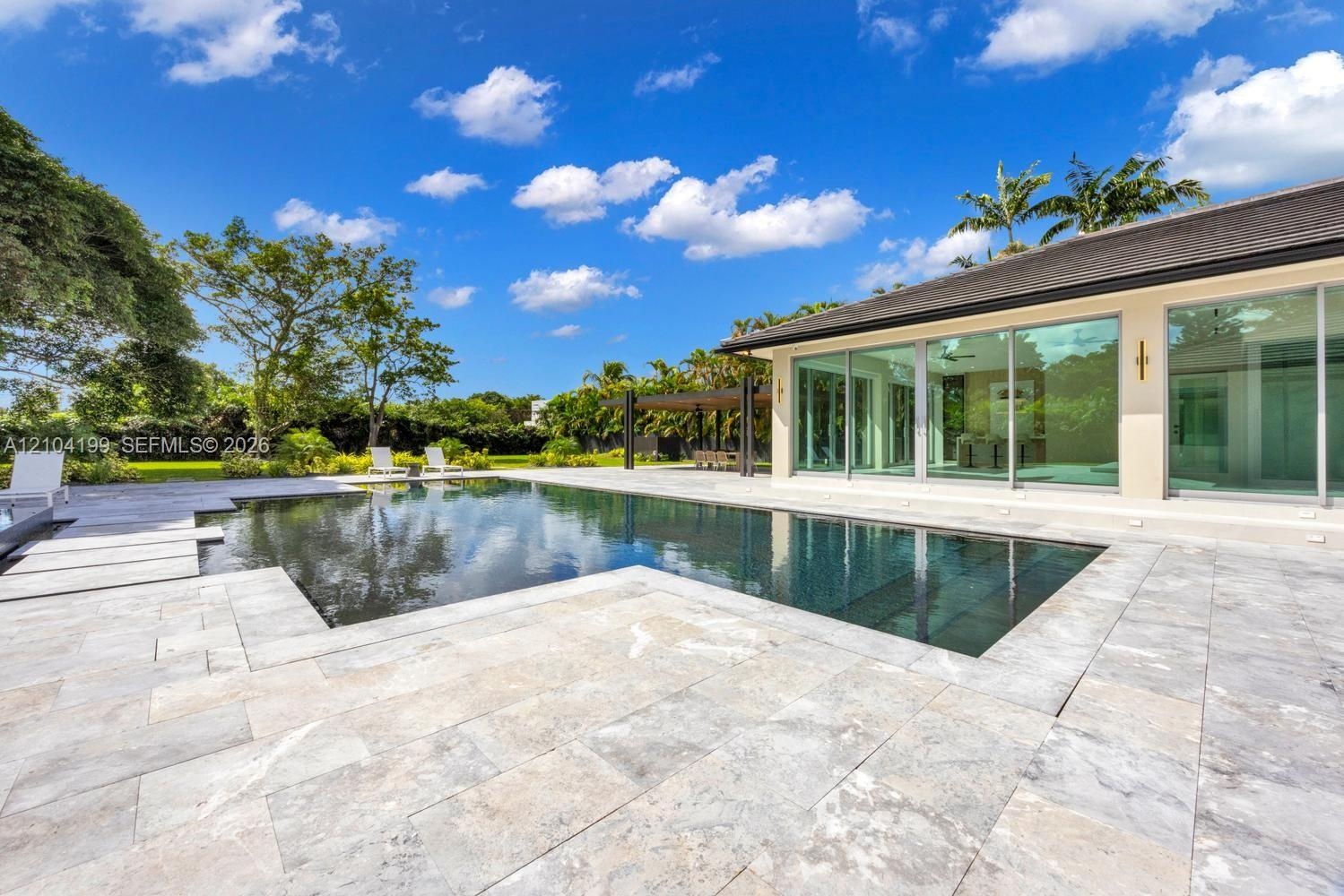 In-ground pool featuring a stone-tile deck, expansive glass sliding doors, and a covered patio area
