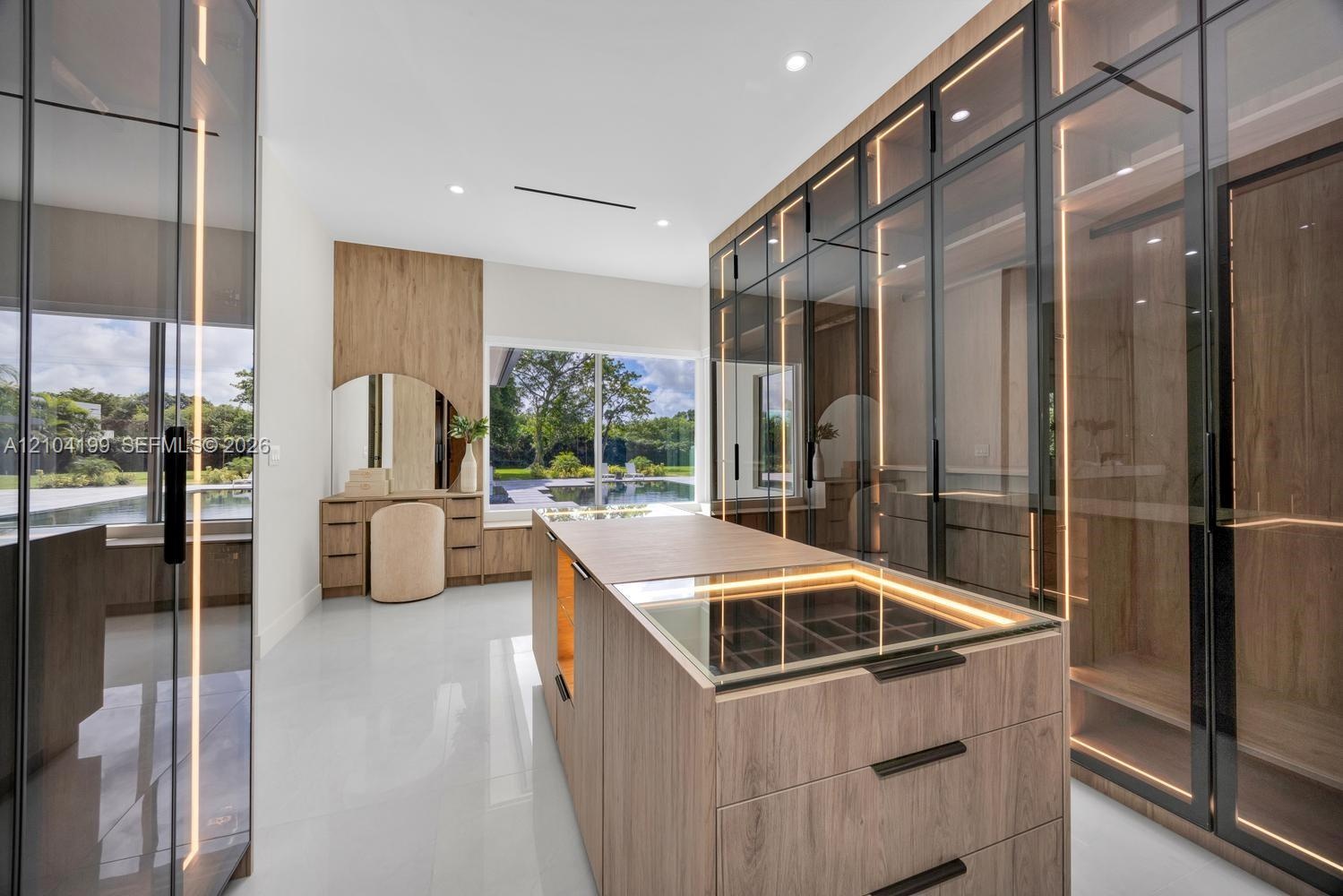 Custom built-in wood-finish cabinetry with full-height glass doors, integrated vertical LED accent lighting, central storage island with glass-top dis