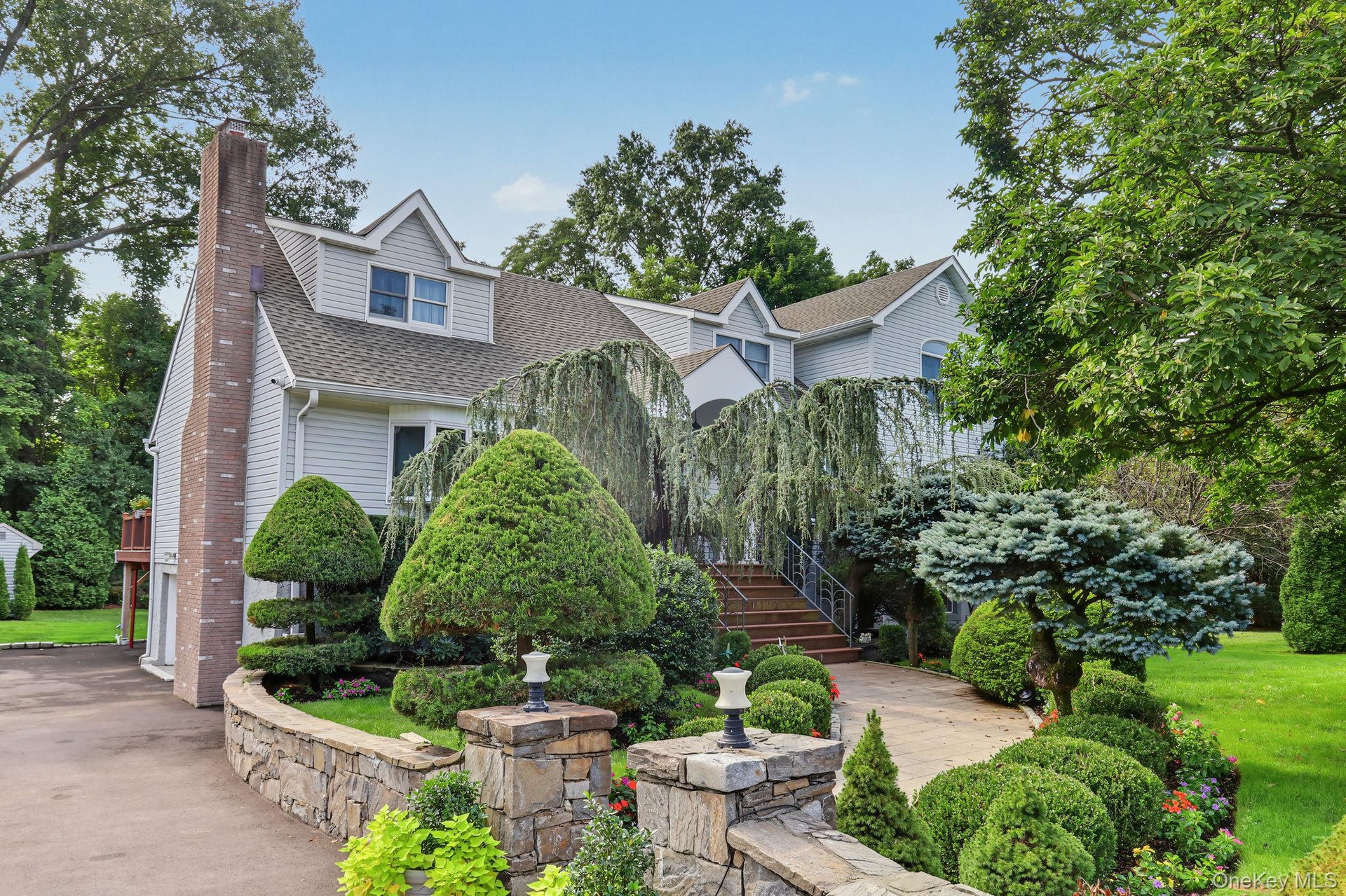 Multi-level exterior featuring light-toned  siding, a masonry chimney, stone retaining walls, structured landscaping, and a paved walkway