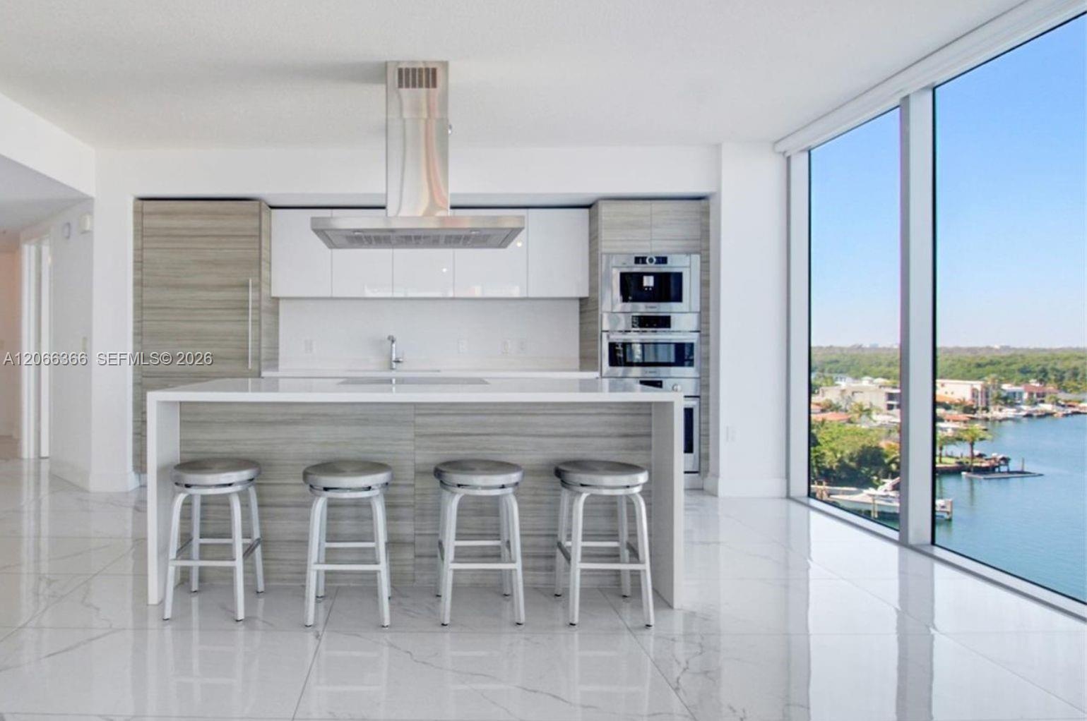 Modern kitchen featuring a waterfall-edge island, high-gloss cabinetry, integrated stainless steel appliances, polished stone-finish flooring, and flo