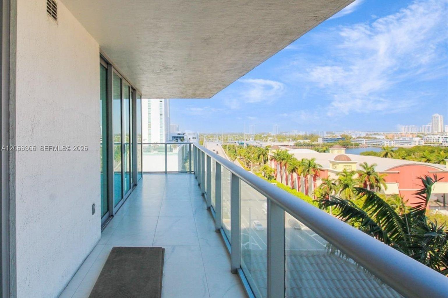 Covered balcony featuring large-format tile flooring, a glass-panel railing, and floor-to-ceiling glass sliding doors