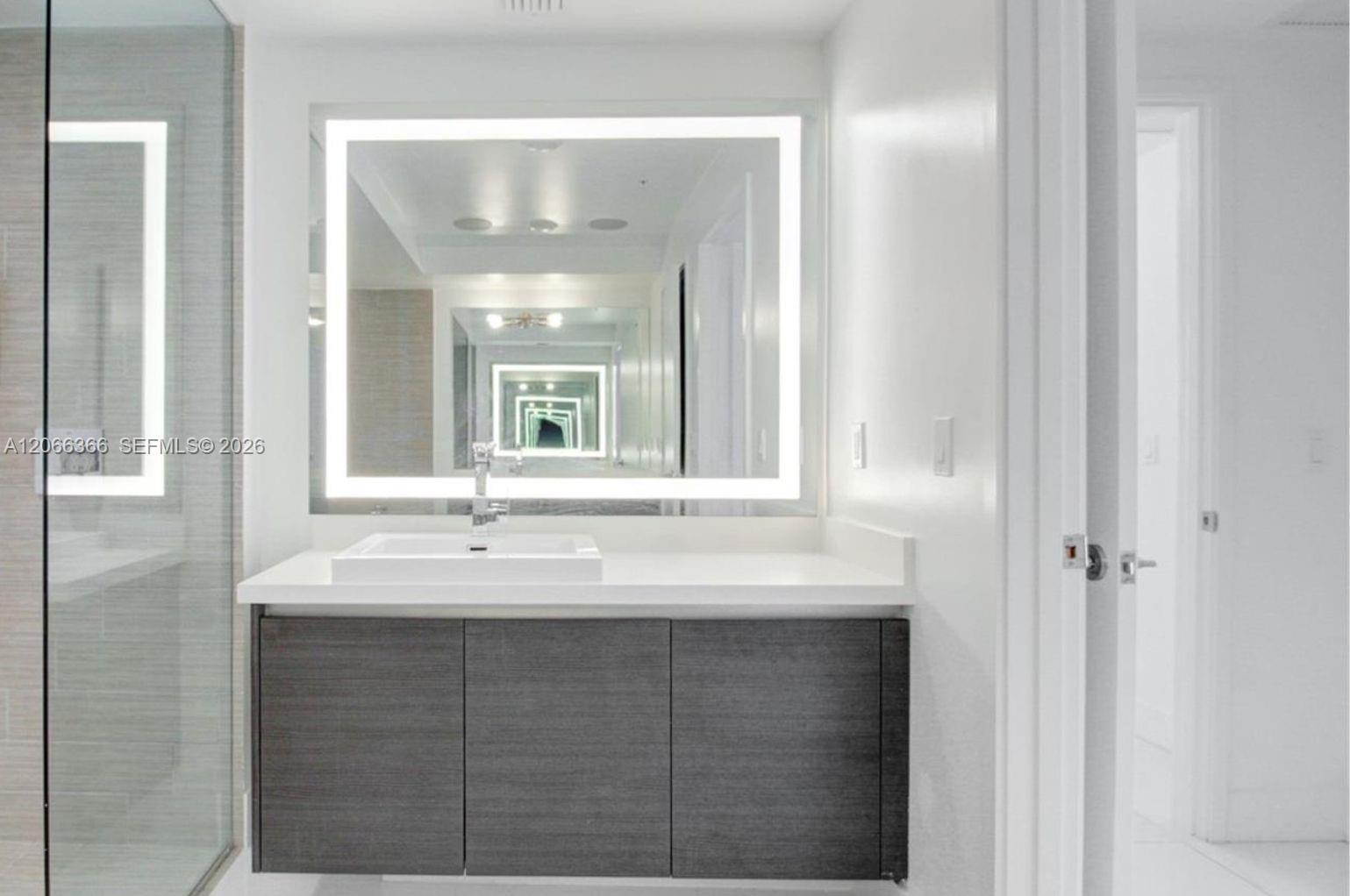 Floating vanity with dark wood-finish cabinetry, white countertop, integrated rectangular sink, wall-mounted faucet, and rectangular LED-backlit mirro