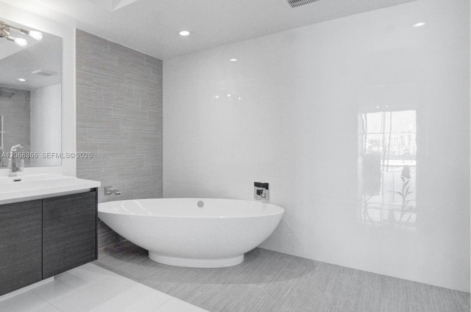 Freestanding oval soaking tub, wall-mounted faucet, custom dark wood-finish vanity with integrated sink, grey textured tile accent wall, and polished 