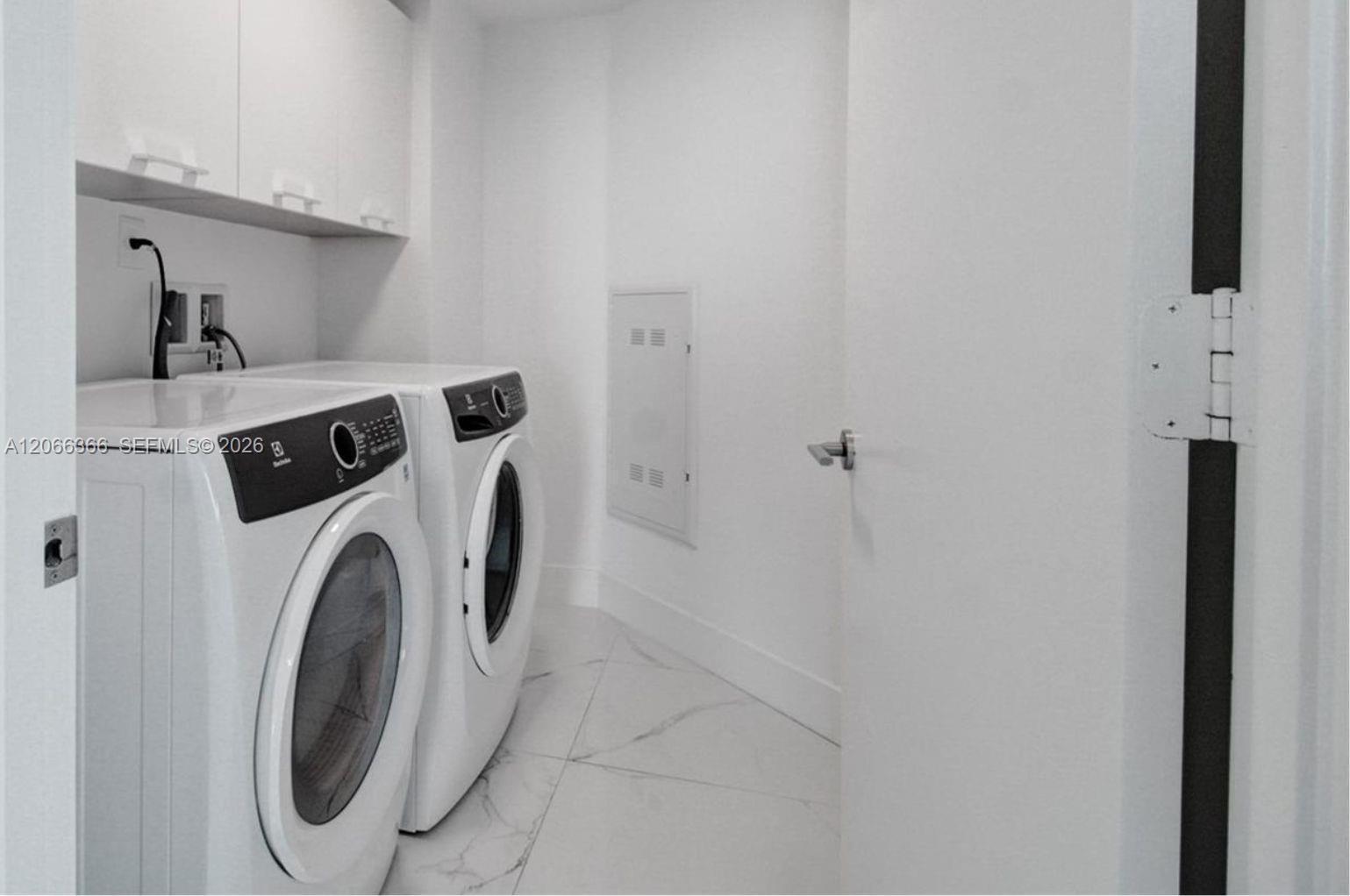 Laundry room featuring white stone-finish tile flooring, built-in upper cabinetry, and a flush-mount utility access panel
