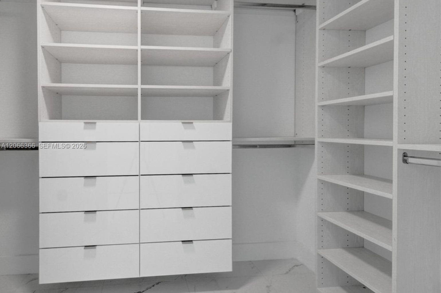 Custom closet system featuring white built-in cabinetry, adjustable open shelving, integrated drawers with metallic pulls, and hanging rods