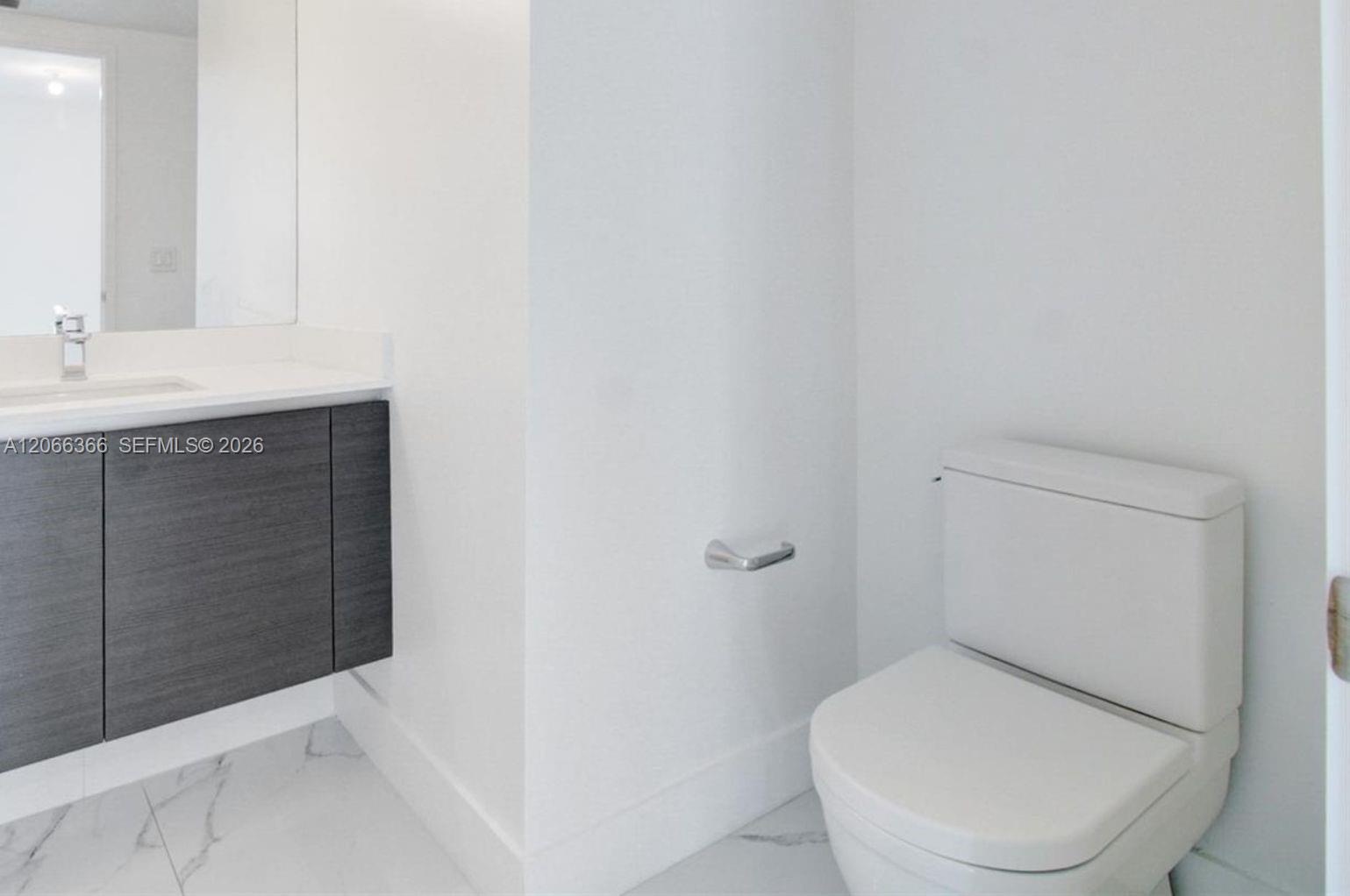 Floating vanity with a dark wood-finish cabinet, stone-finish countertop, undermount sink, and white floor tiling with marble-style veining