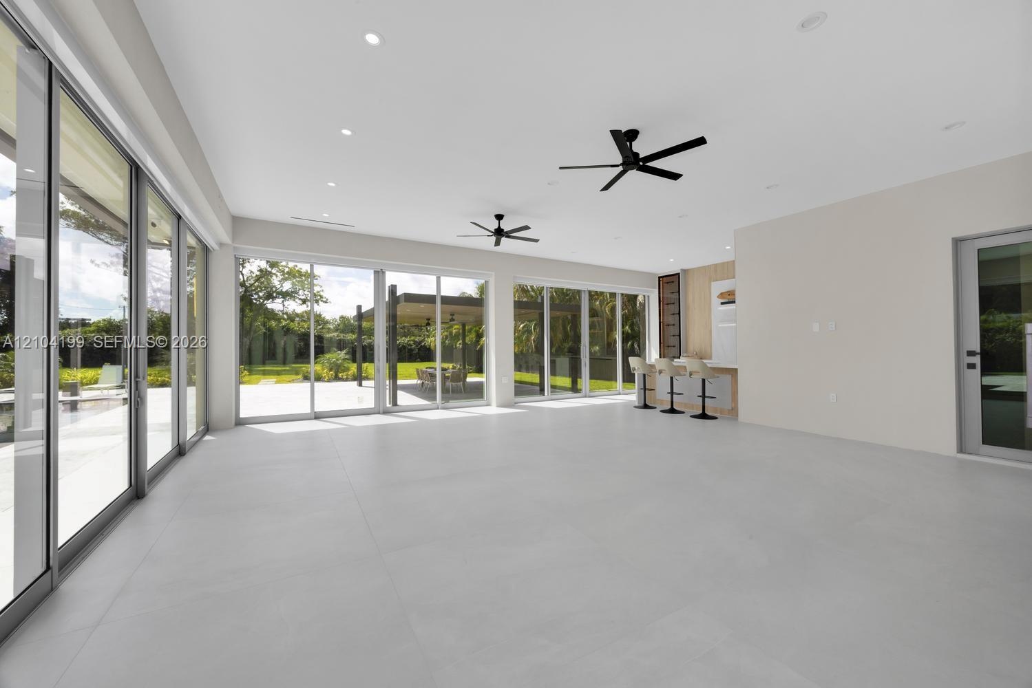 Large-format porcelain tile flooring, expansive floor-to-ceiling sliding glass doors, built-in wet bar with wood-panel detailing, recessed lighting, a