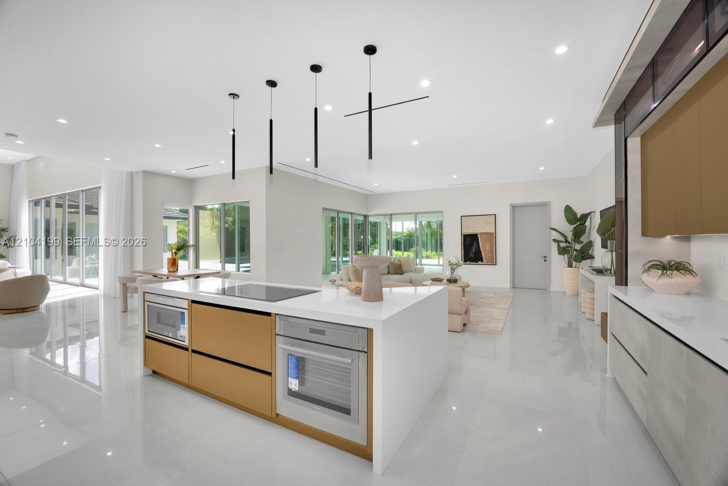 Modern kitchen featuring a central island with integrated cooktop and oven, sleek flat-panel cabinetry, light-toned stone-surface countertops, recesse