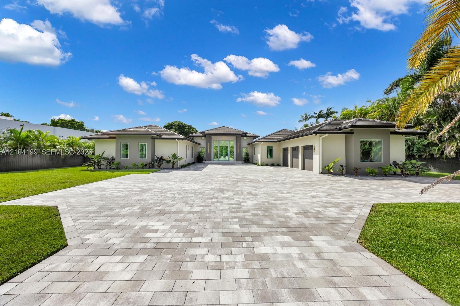Contemporary single-story exterior featuring a paver stone driveway, multi-car garage, manicured lawn, and full-height glass entryway