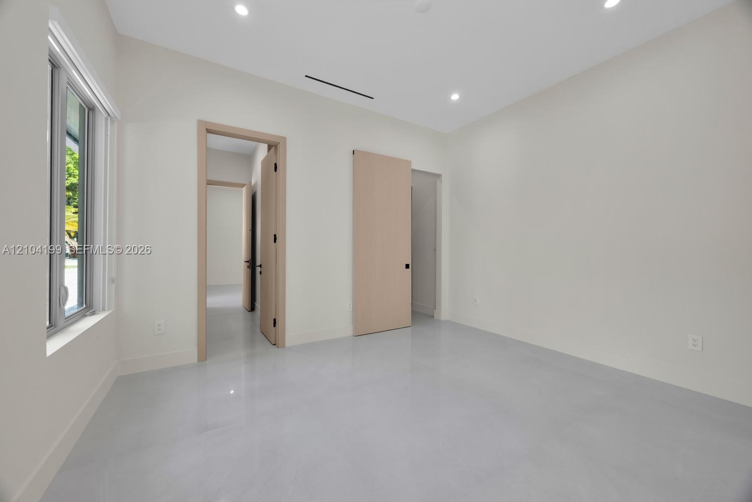 Neutral-toned room featuring smooth concrete-finish flooring, recessed lighting, light-wood interior doors, and a sliding barn-style door