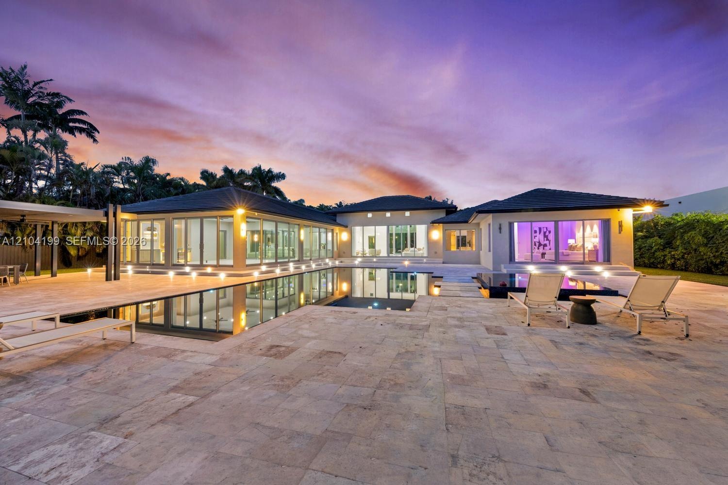 Single-story residence featuring an expansive stone-paved patio, an infinity-edge swimming pool, extensive floor-to-ceiling glass wall panels, and rec