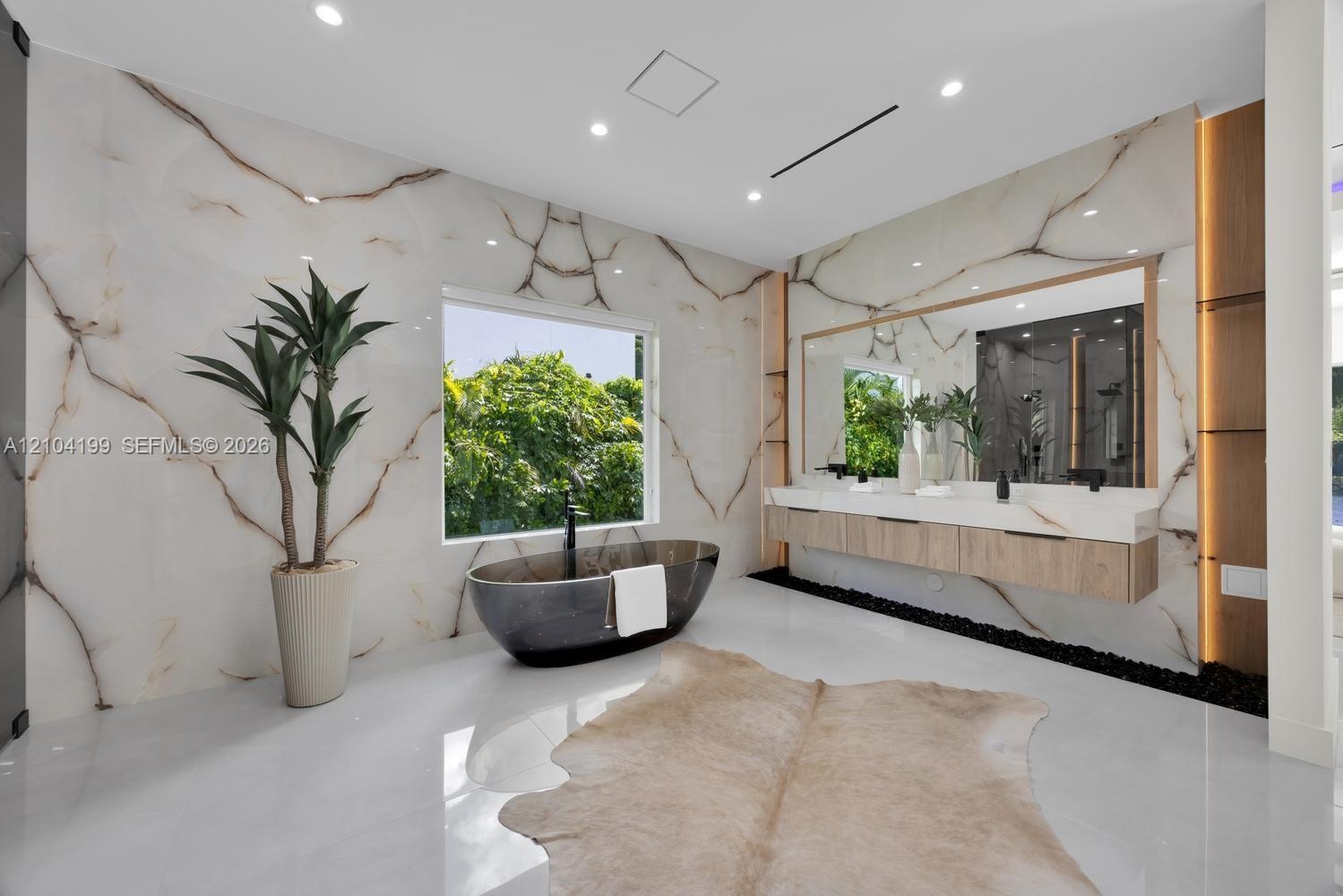 Full-height stone wall cladding with vein detailing, a freestanding dark basin soaking tub with wall-mounted plumbing, a dual-vanity floating cabinet 