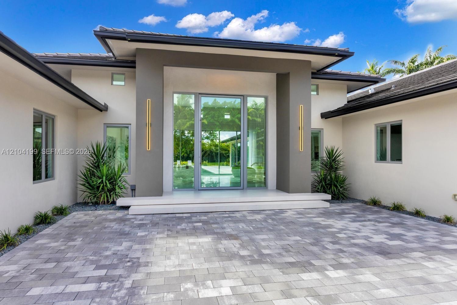 Modern architectural exterior featuring a paved stone driveway, recessed entry with a double-height frame, full-height glass entryway, and vertical wa
