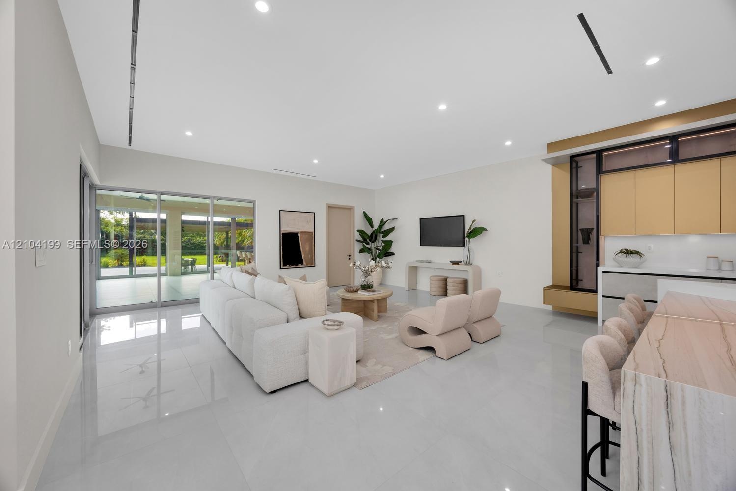 Open-concept living space featuring large-format tile flooring, recessed linear lighting, sliding glass walls, and custom cabinetry with stone-surface