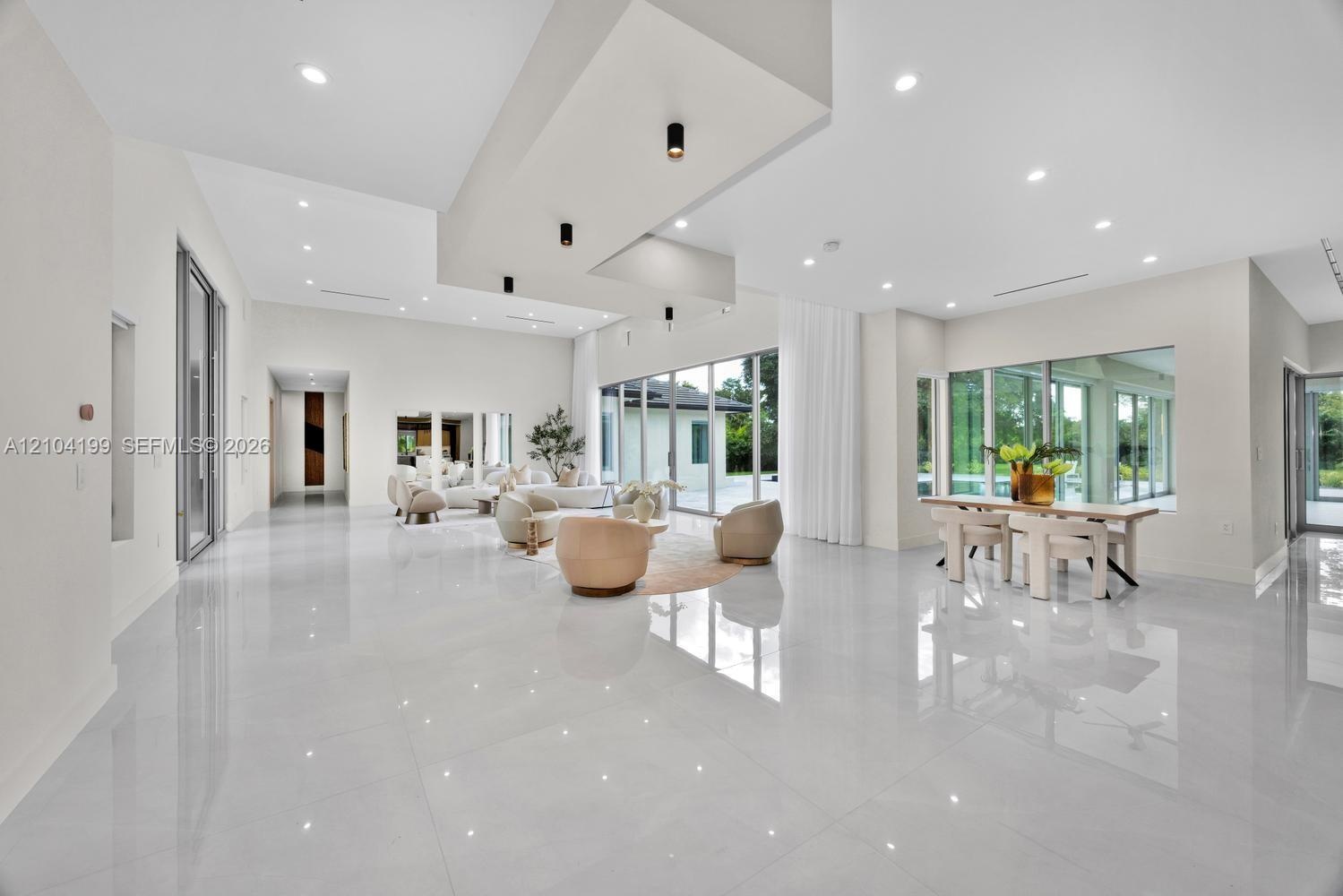 Open-concept living space featuring high-gloss tile flooring, recessed lighting, a tiered tray ceiling with cylindrical pendant fixtures, and floor-to