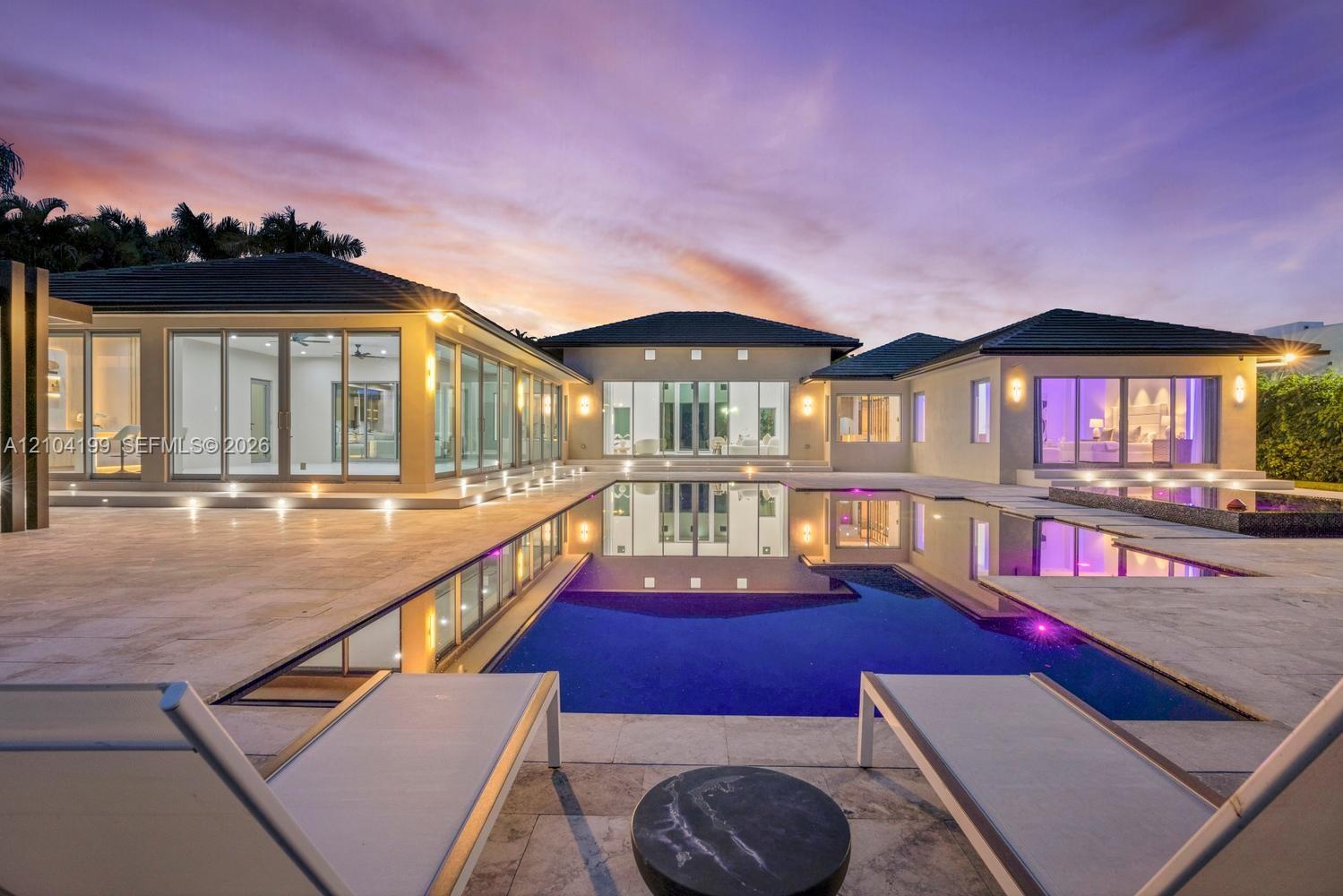 Exterior featuring an expansive stone patio, a multi-section swimming pool with integrated spa, floor-to-ceiling glass wall systems, and low-profile r