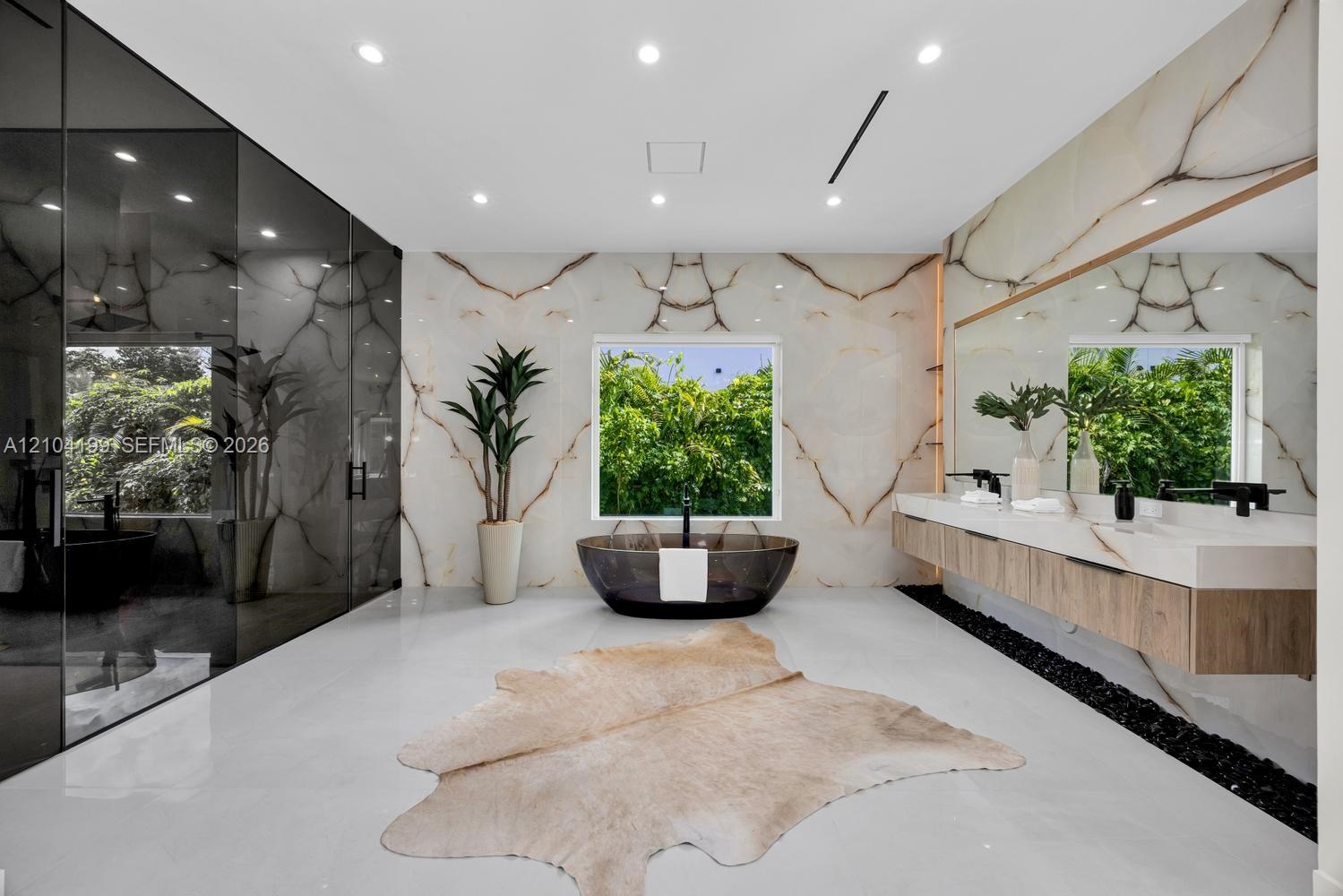 Full-wall stone slab surrounds, floating wood-finish dual vanity with integrated countertop, dark soaking tub, recessed ceiling lighting, and polished