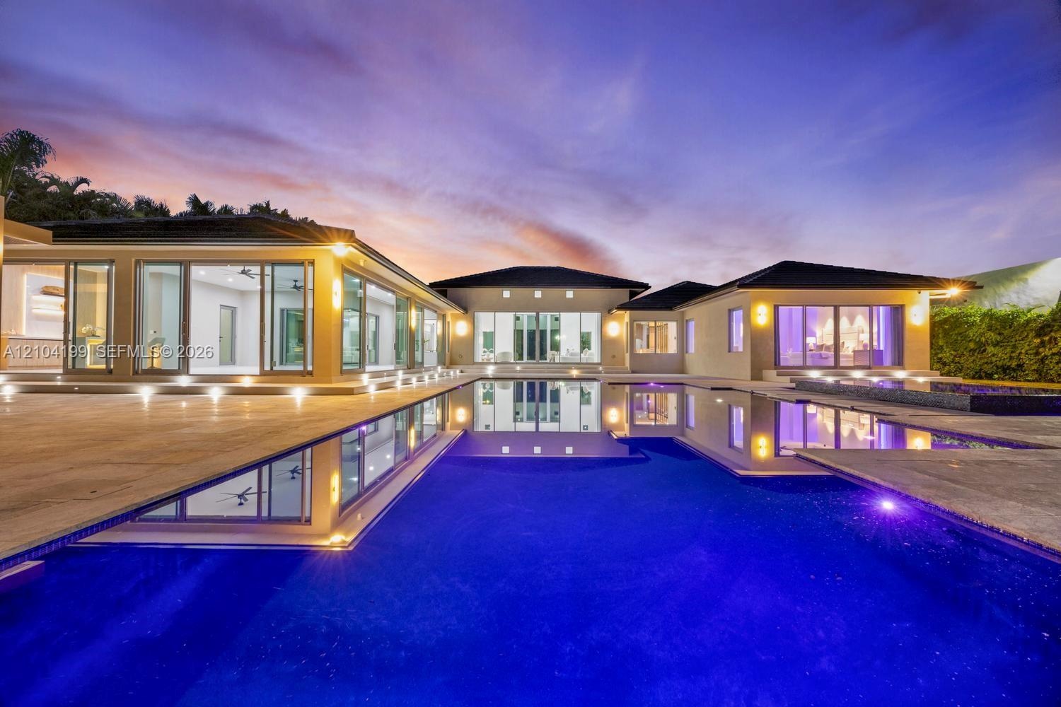 Contemporary residence featuring an infinity-edge pool, stone-paved patio, recessed exterior lighting, and floor-to-ceiling glass sliding doors