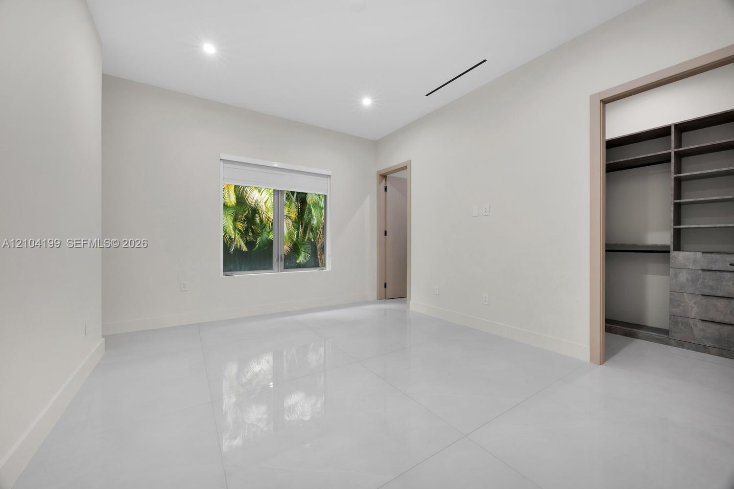 Neutral-toned interior featuring large-format tile flooring, recessed lighting, and a walk-in closet equipped with custom built-in shelving and drawer