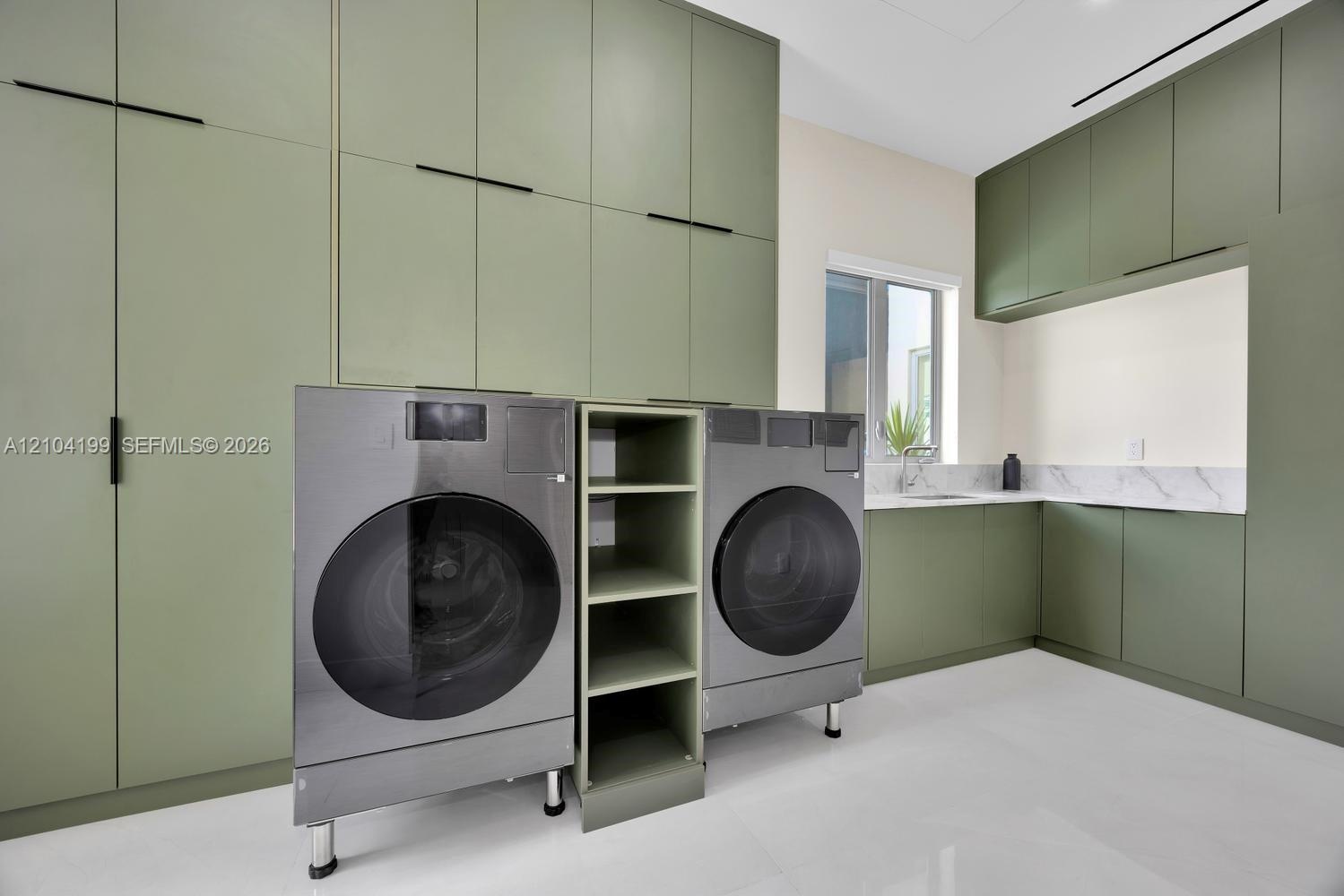 Full-height sage green cabinetry with matte black hardware, stone-surface backsplash, integrated shelving, and white tile flooring