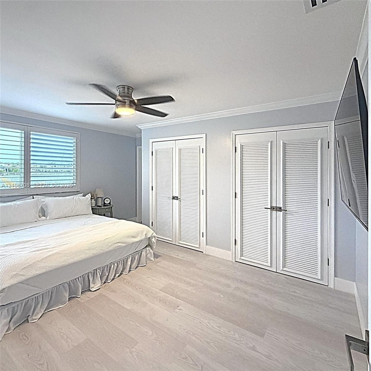 Wood-finish flooring, dual sets of louvered closet doors with matte black hardware, and a ceiling-mounted light fixture with integrated fan blades